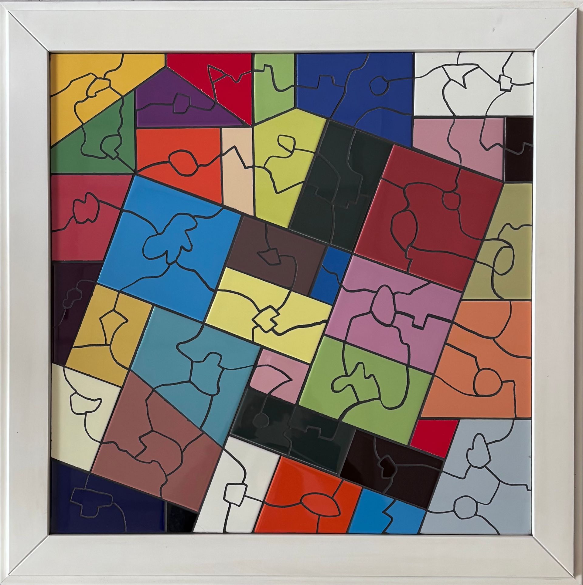 Kleurrijk abstract puzzelkunstwerk met in elkaar grijpende geometrische stukken in een zilveren lijst.