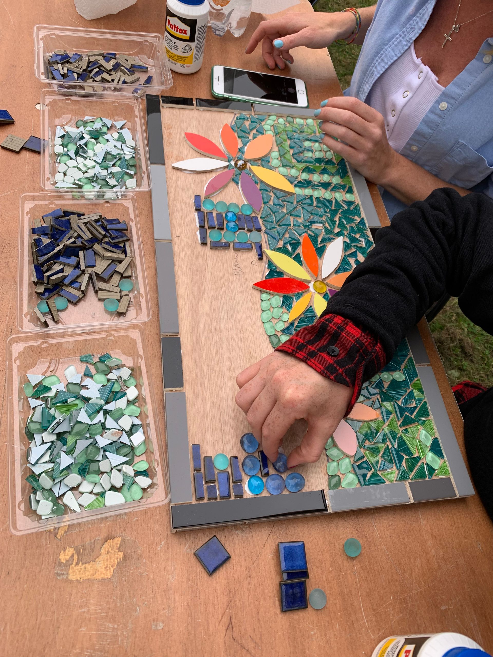 Mensen maken op een tafel een kleurrijke mozaïekbloemencollage met tegels en lijm.