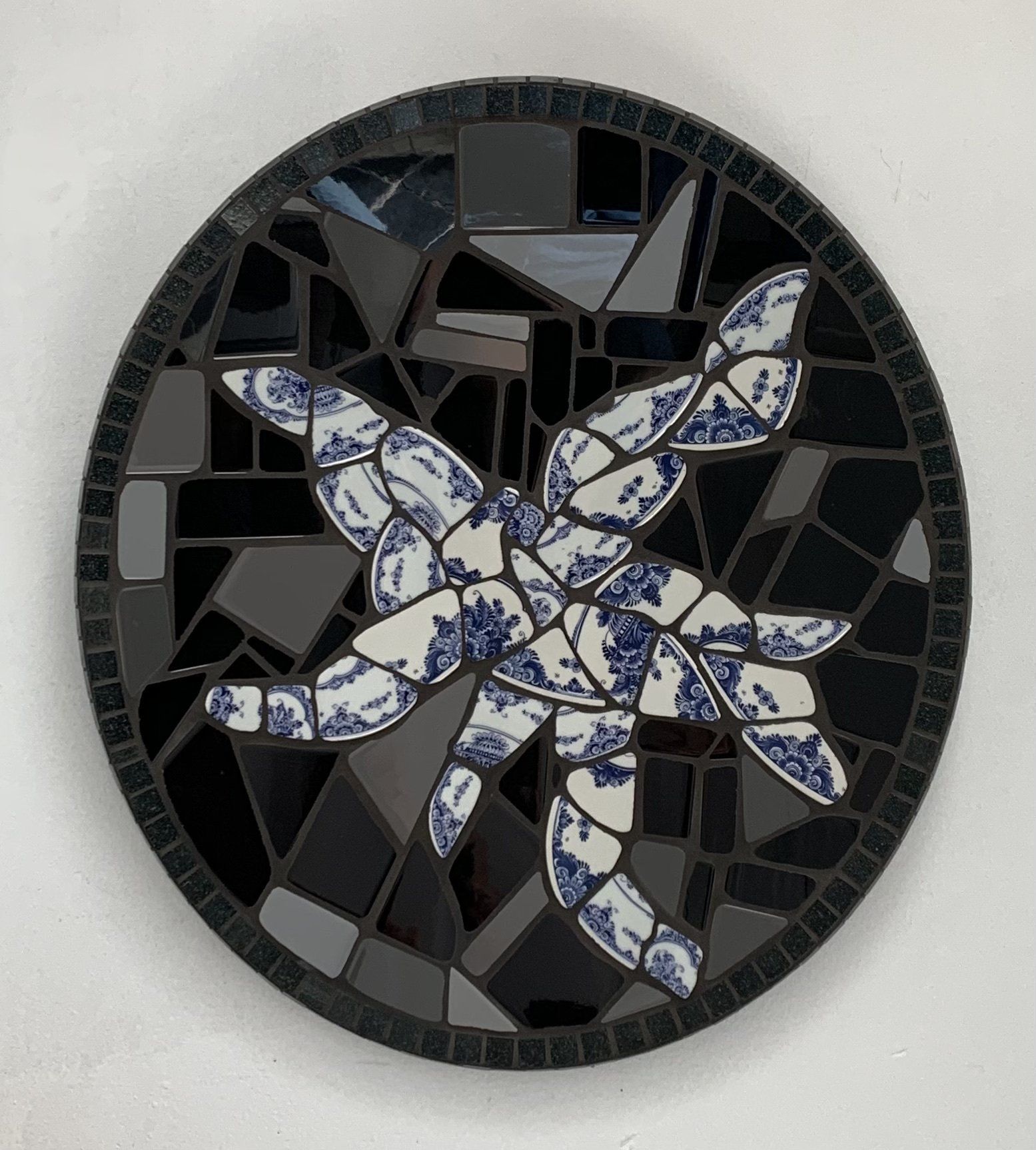 Rond mozaïek met blauw-witte zeesterren op een zwarte achtergrond.
