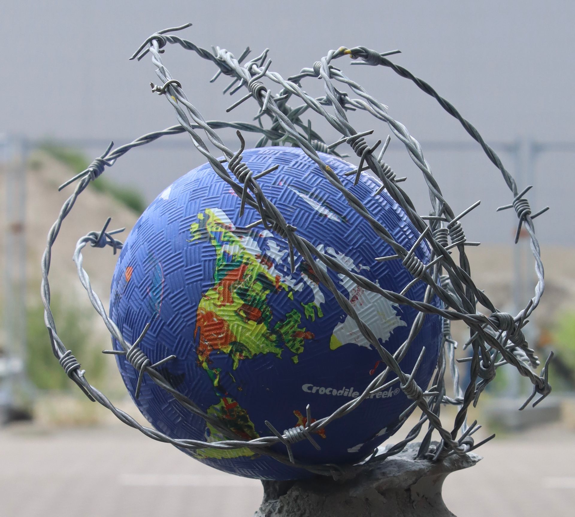Een blauwe wereldbol omwikkeld met prikkeldraad, symbool voor wereldwijd conflict en opsluiting.