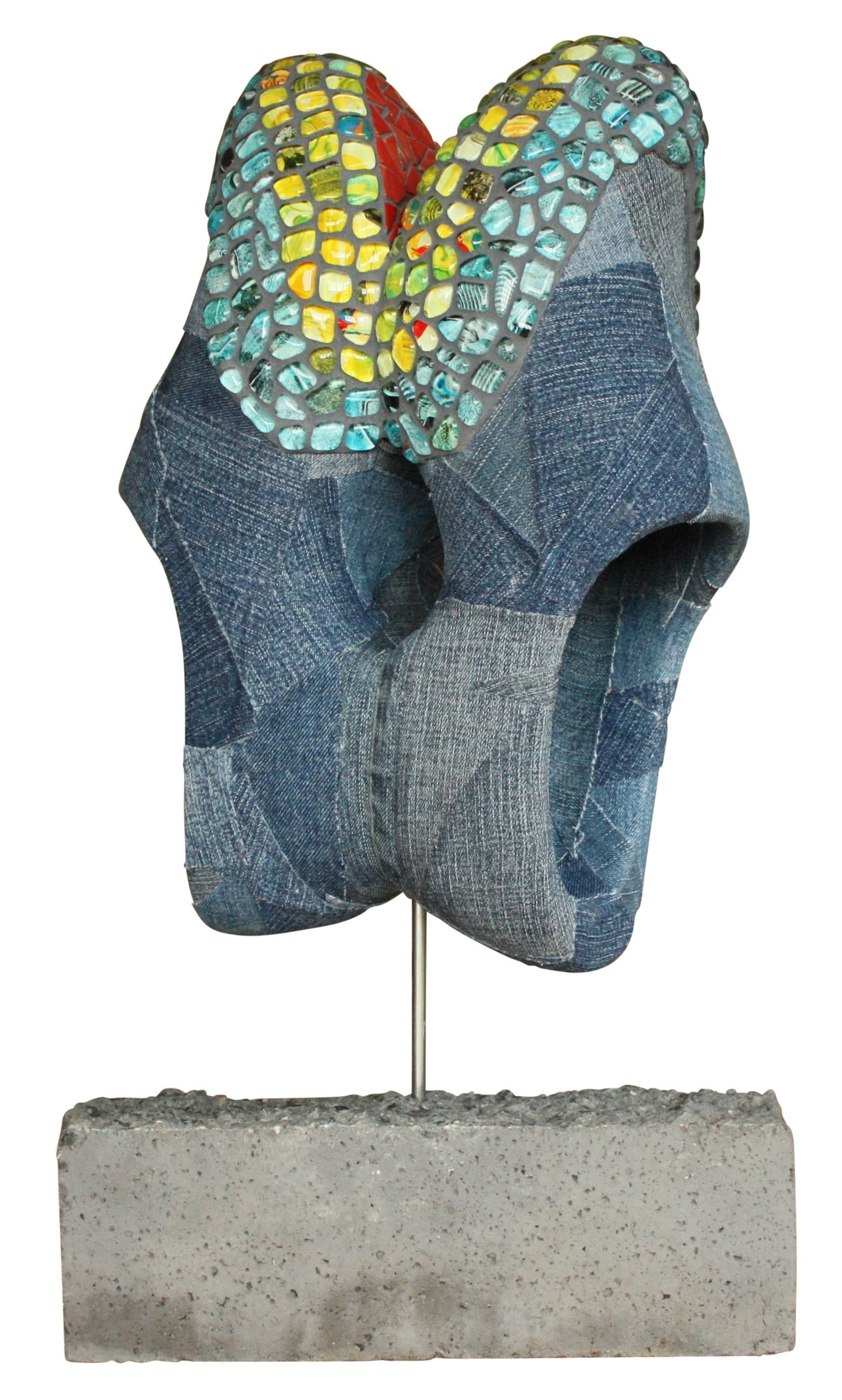 Abstracte blauw-gele mozaïeksculptuur op een dunne sokkel boven een betonnen voetstuk.