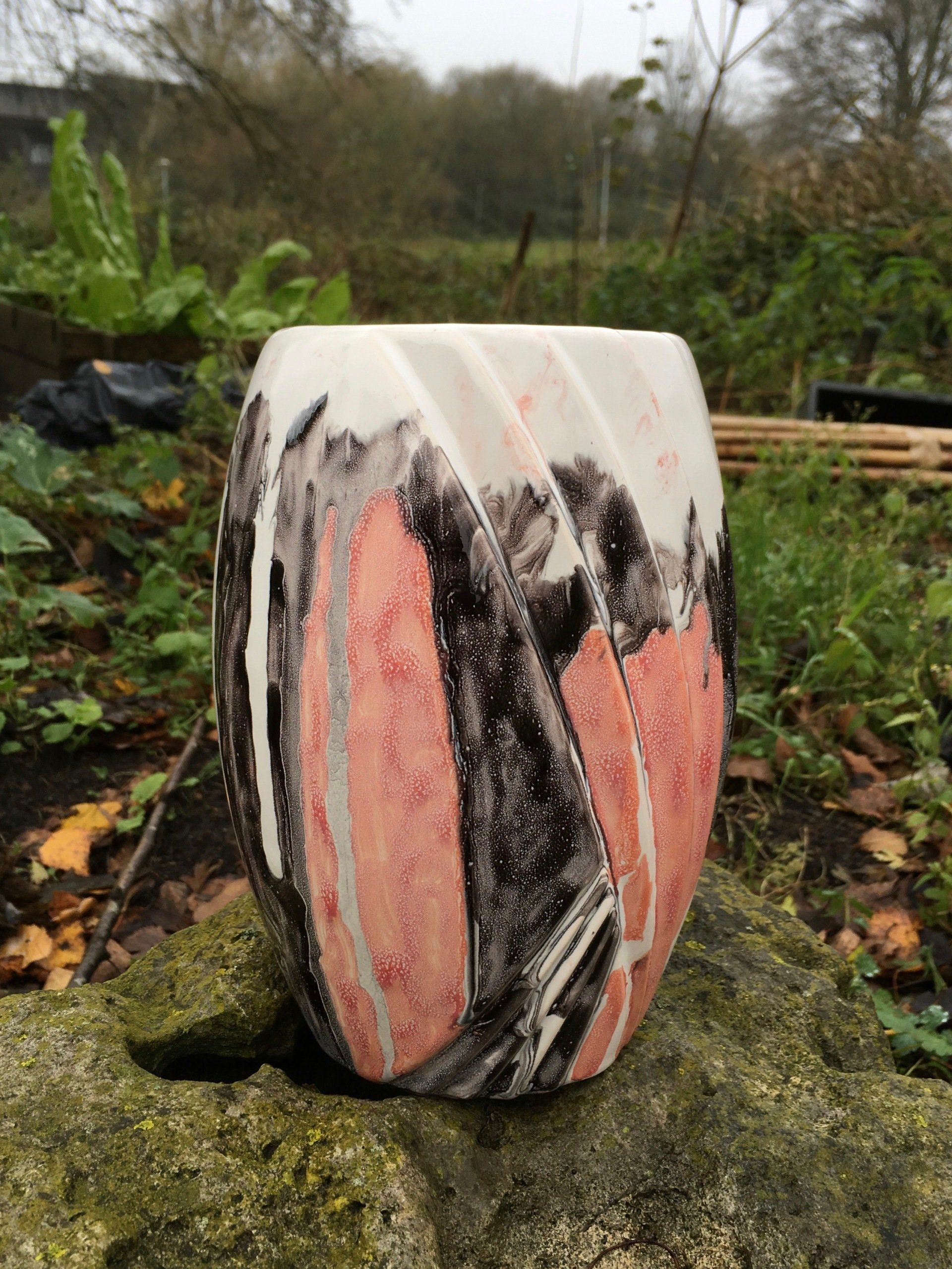 Abstracte, beschilderde keramische vaas met roze, zwarte en witte marmering, buiten op een mosachtige ondergrond.