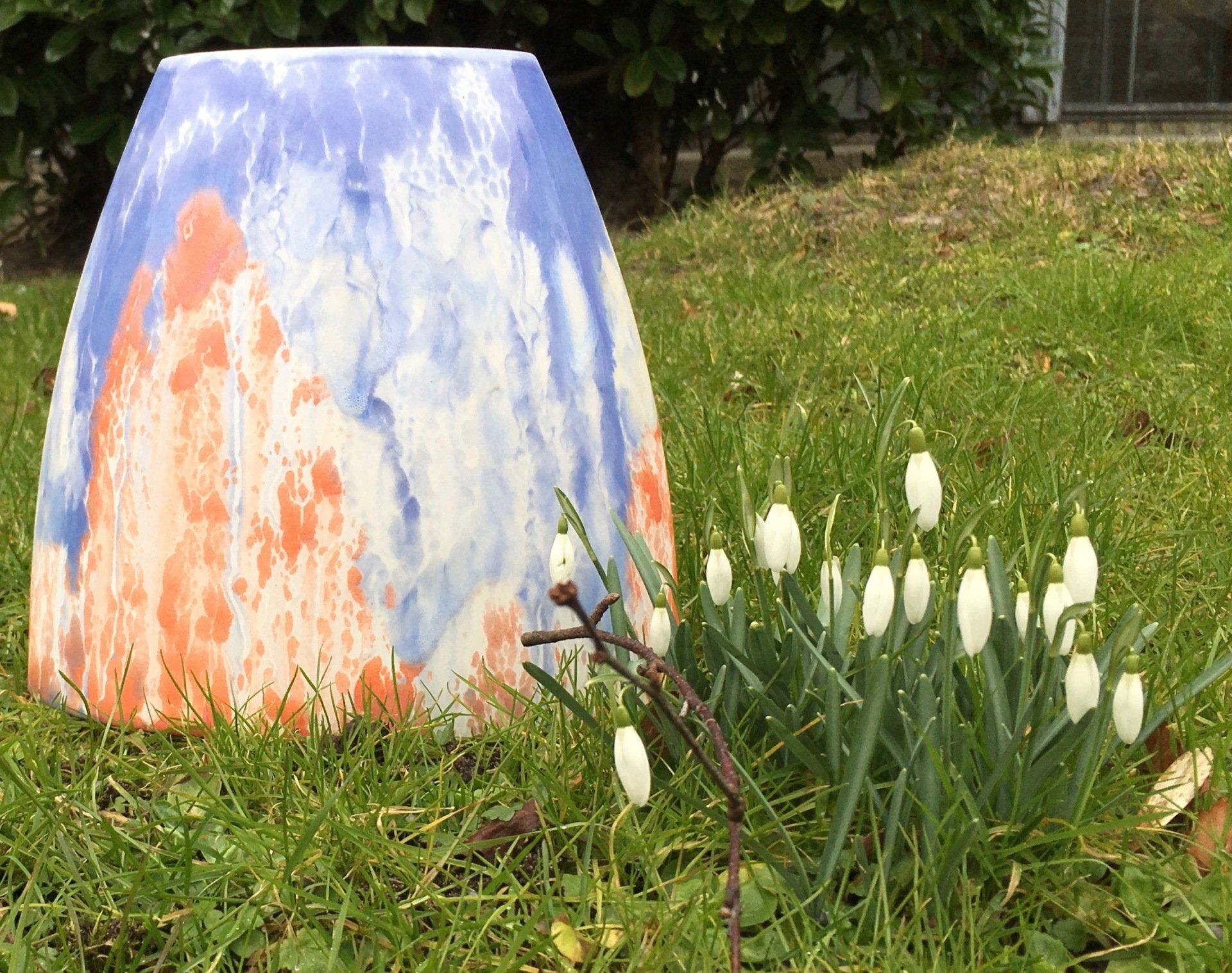 Geschilderd tuinbeeld naast witte bloemen op een grasveld.