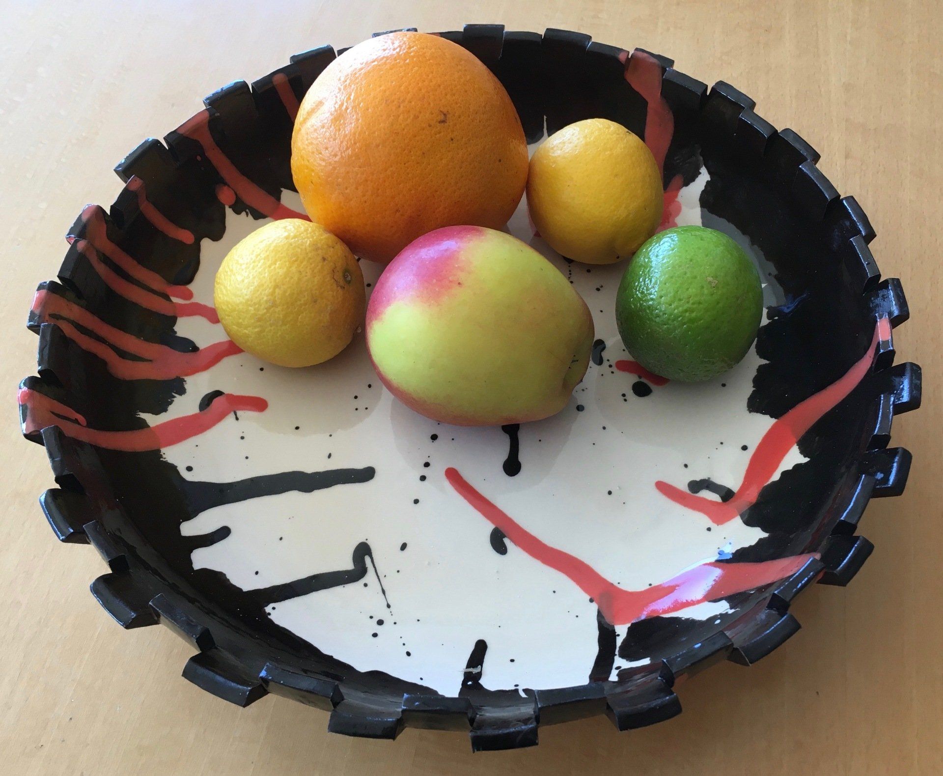 Een zwarte schaal met vijf kleurrijke vruchten op een tafelblad.