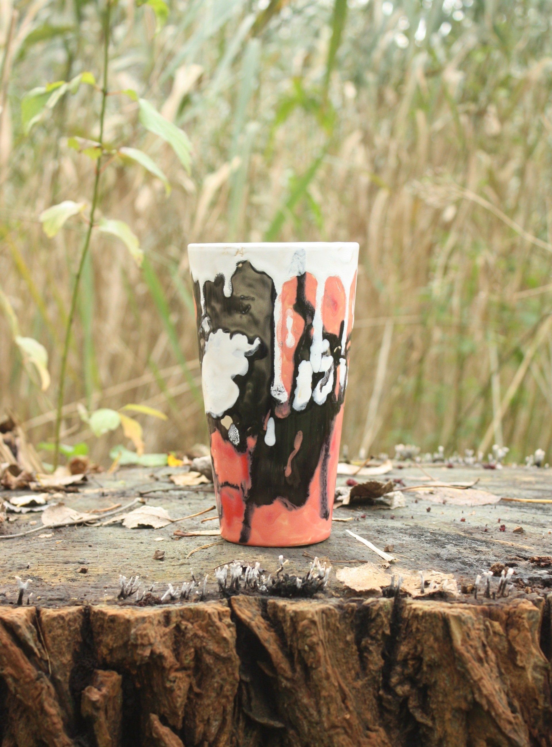 Beschilderde beker met abstracte zwart-wit- en koraalkleurige patronen op een boomstronk in de buitenlucht