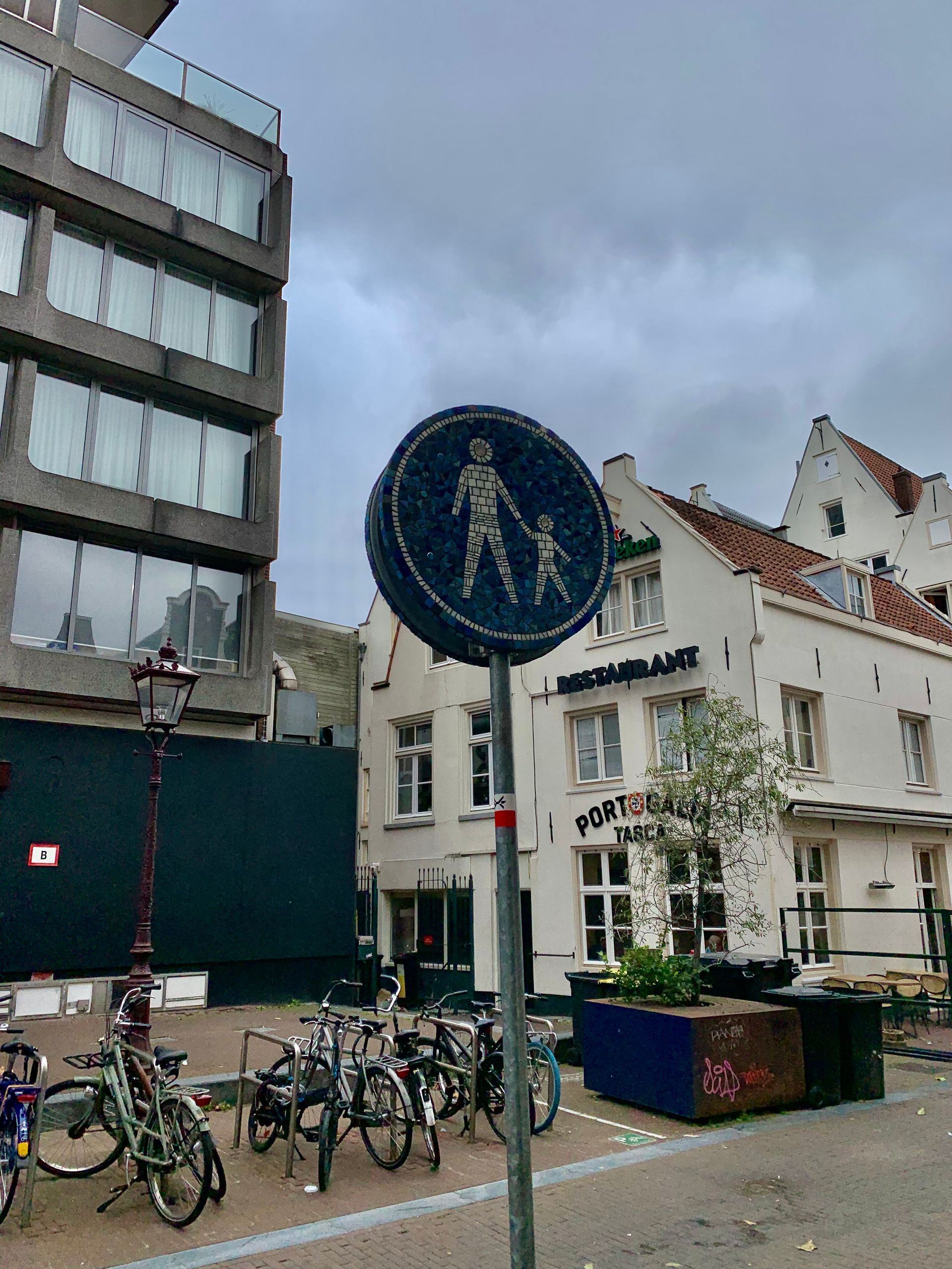 Een stadsstraat met fietsen, een blauw verkeersbord en witte gebouwen onder een bewolkte hemel.