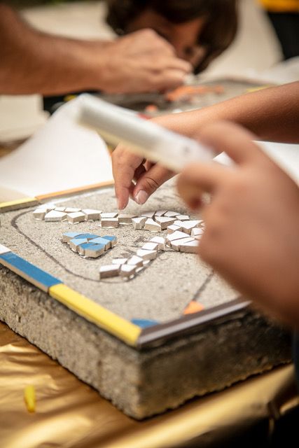 Handen die een mozaïekontwerp samenstellen op een werktafel met gereedschap en een wazige achtergrond.