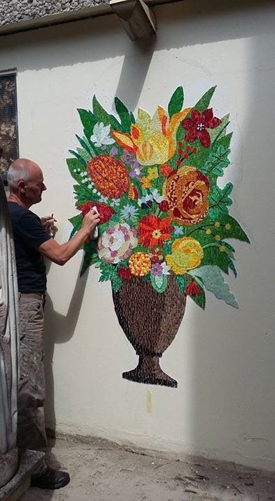 Een man schildert een kleurrijke bloemenmuur op een buitenmuur.