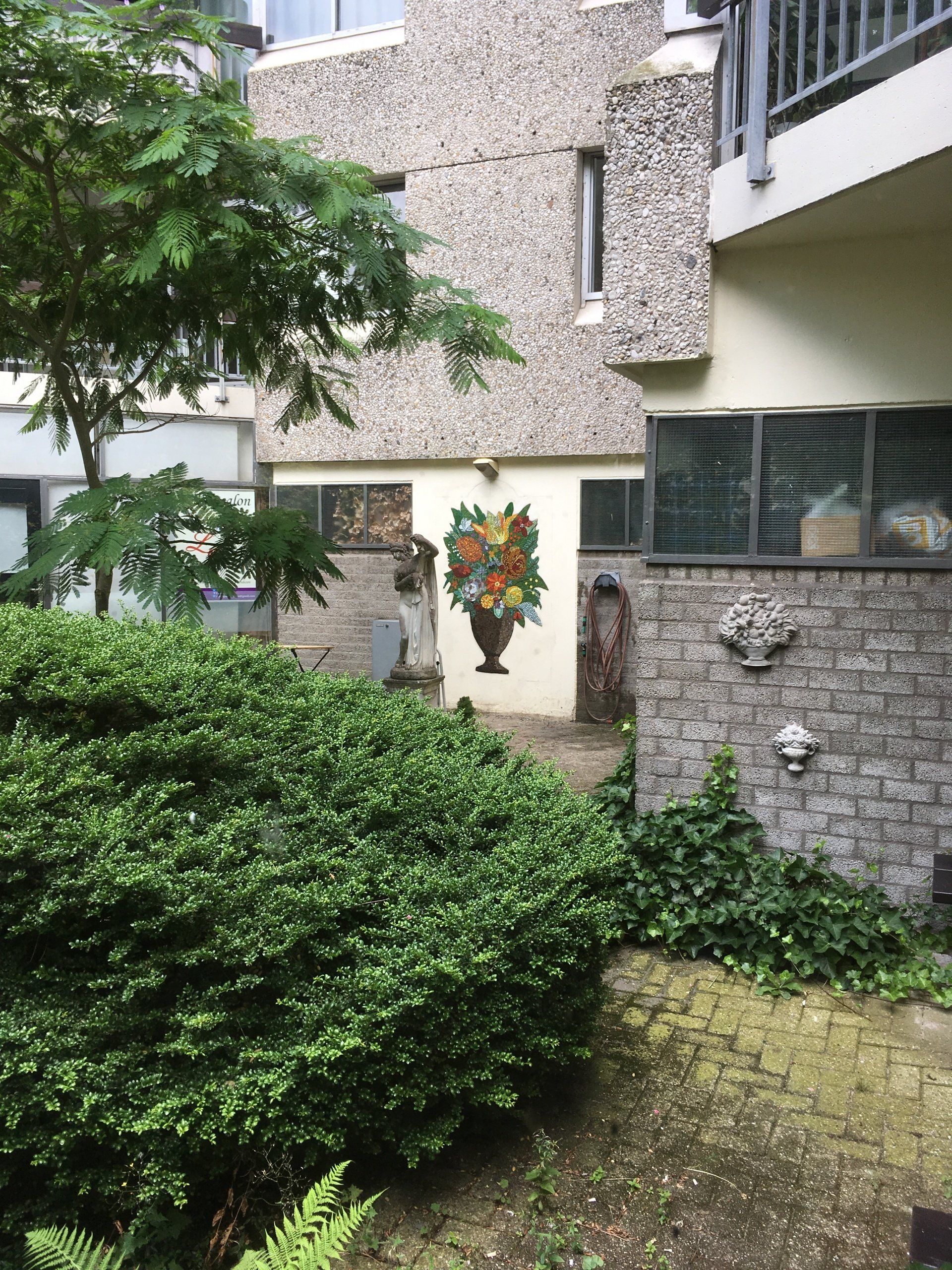 Binnenplaats met weelderige groene struiken, stenen muren en een versierde deuropening onder een balkon.