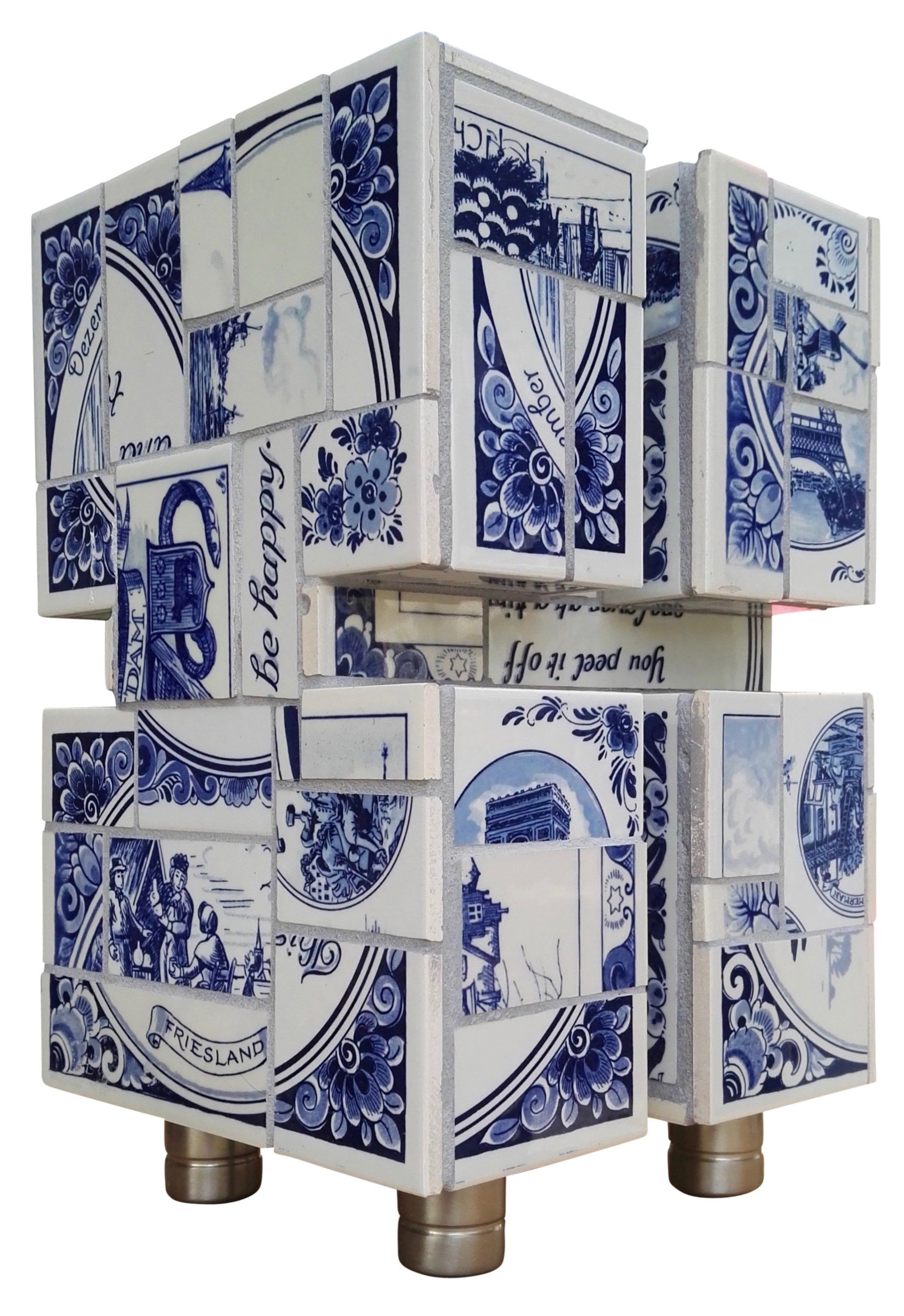 Blauw-witte kubussculptuur op vier kleine metalen pootjes, met sierlijke bloem- en geometrische patronen.
