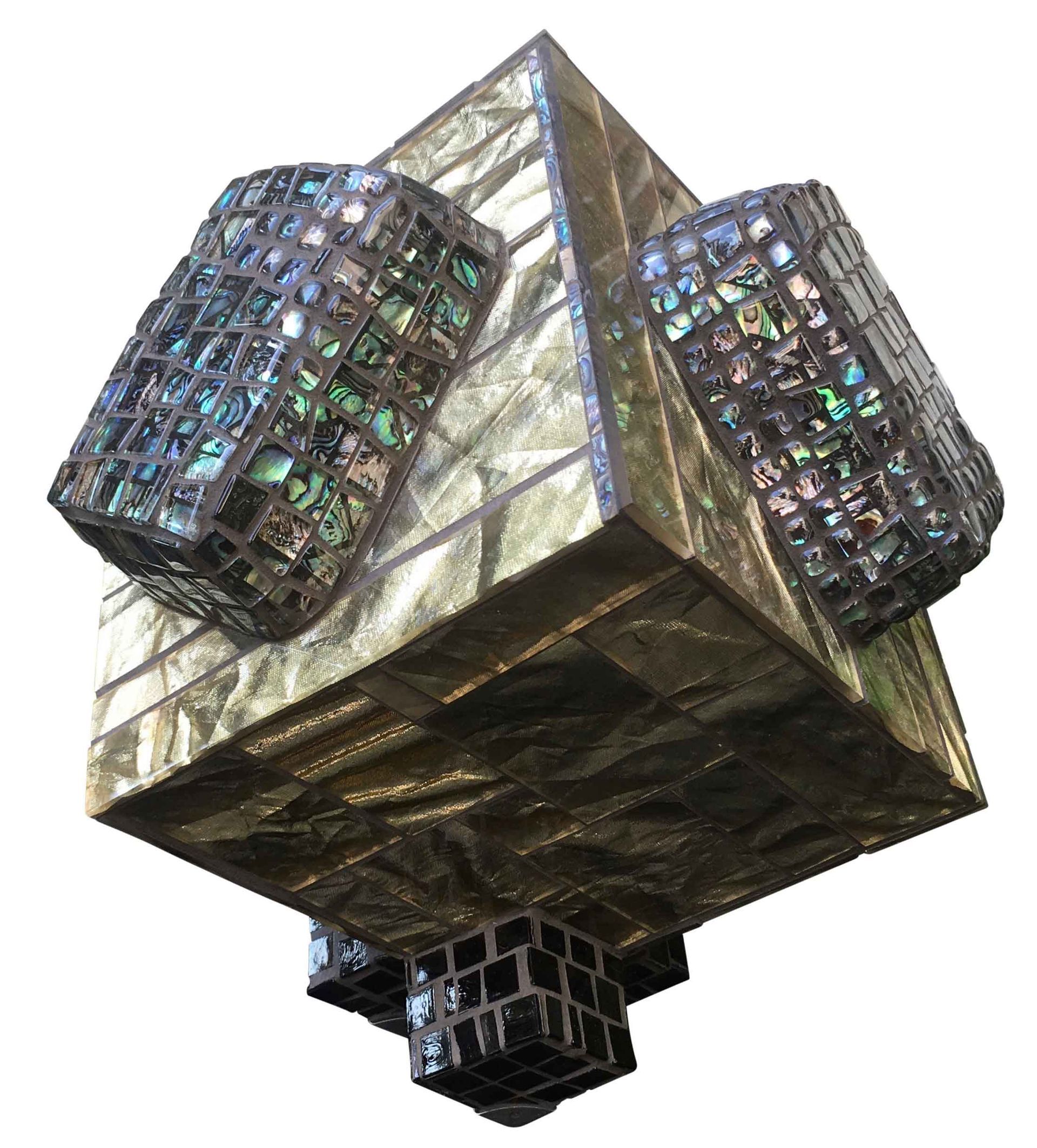 Abstracte metalen sculptuur met een gouden piramide in het midden en donkere, reflecterende kubusvormige uitsteeksels.