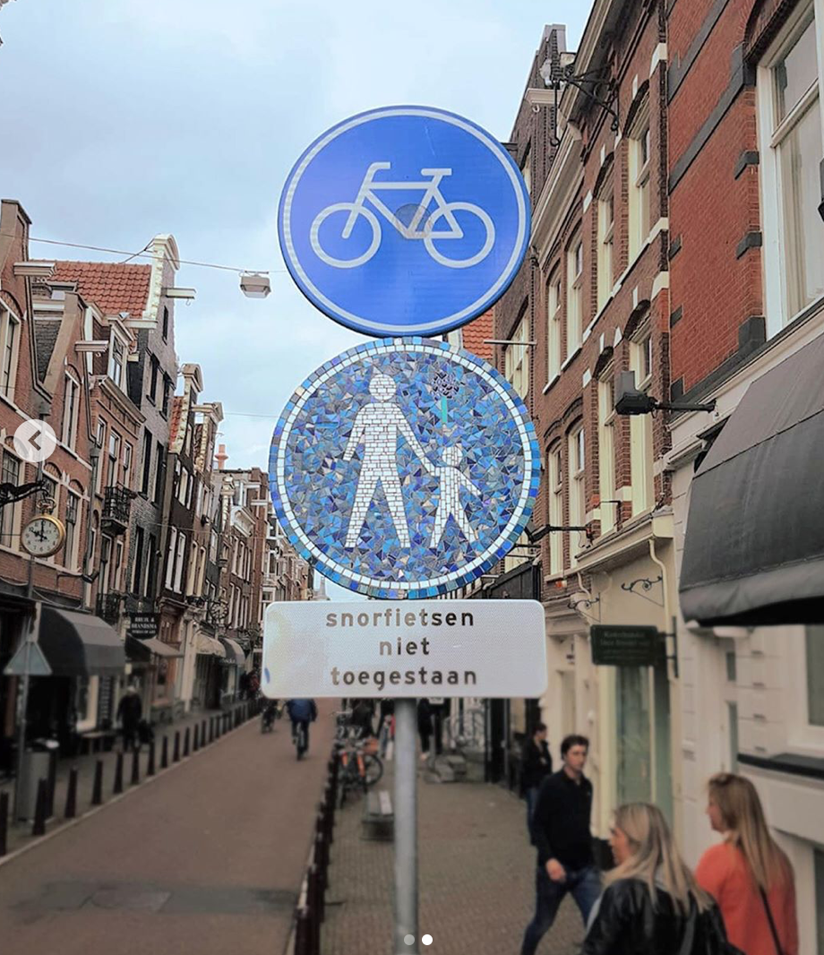 Blauwe borden met een verbod voor fietsers en voetgangers in een smalle straat, met daaronder Nederlandse tekst.