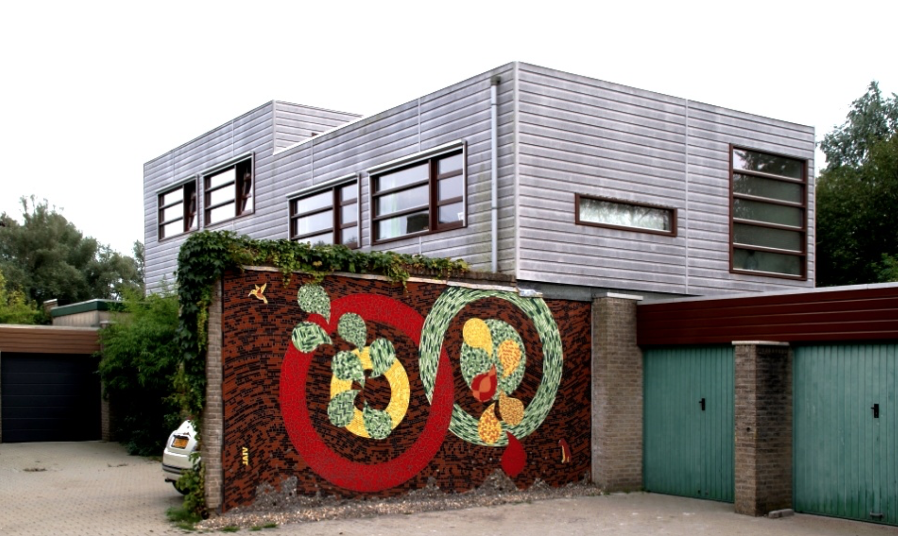 Modern huis met zilverkleurige bovengevel en kleurrijke muurschildering op een bakstenen muur naast een garage.