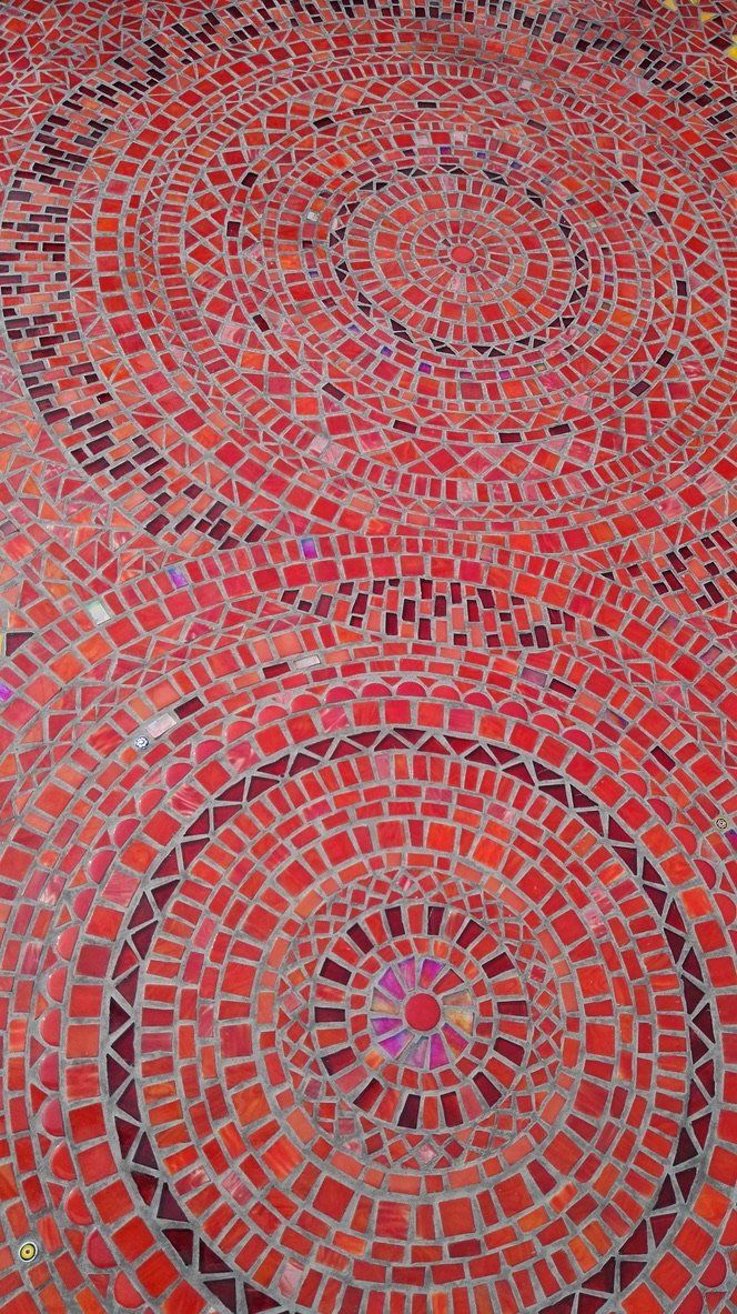 Abstracte mozaïek in rood en grijs met twee concentrische cirkelvormige patronen.