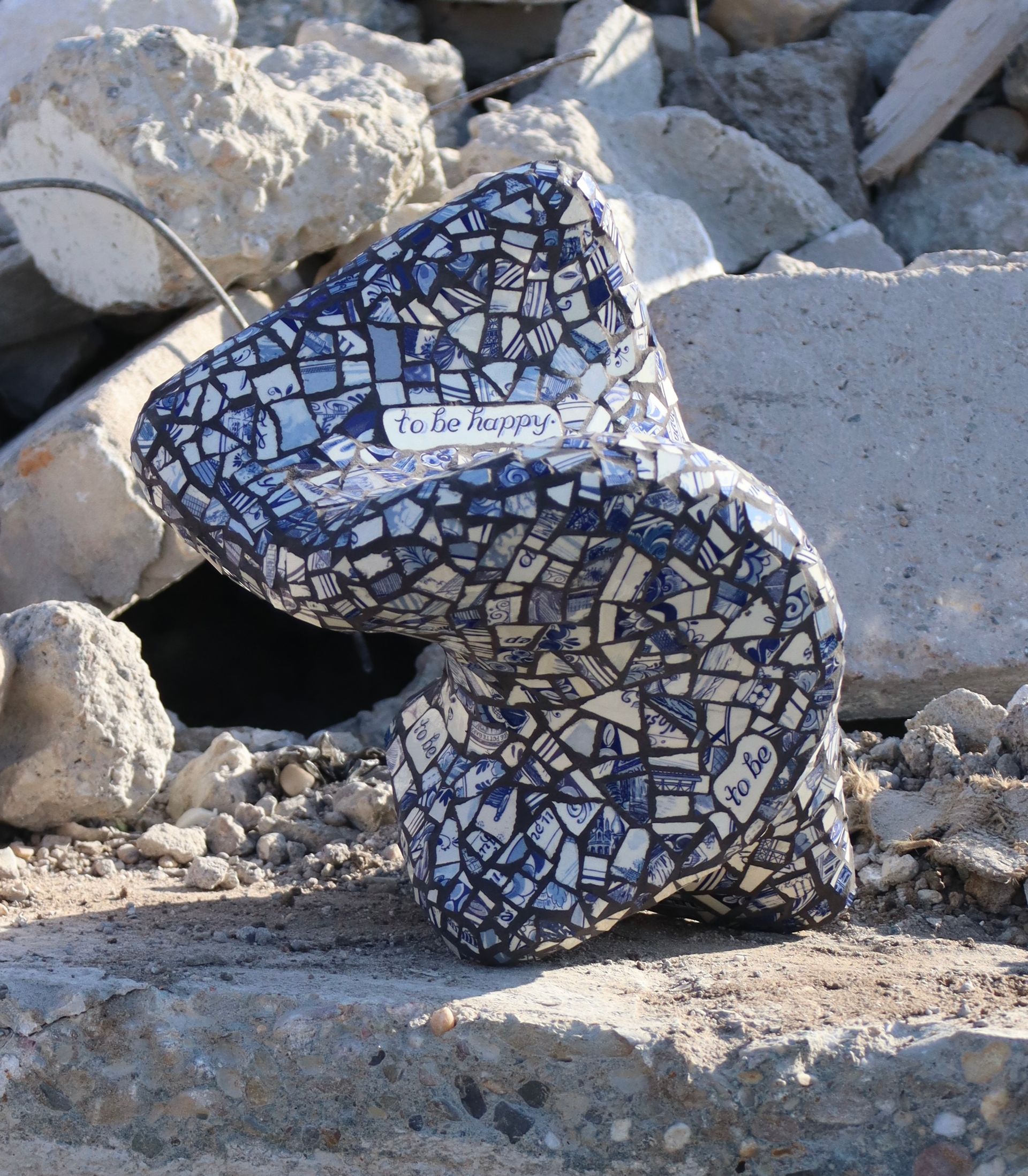 Blauw-wit mozaïeksculptuur in de vorm van een S te midden van grote rotsen en puin.