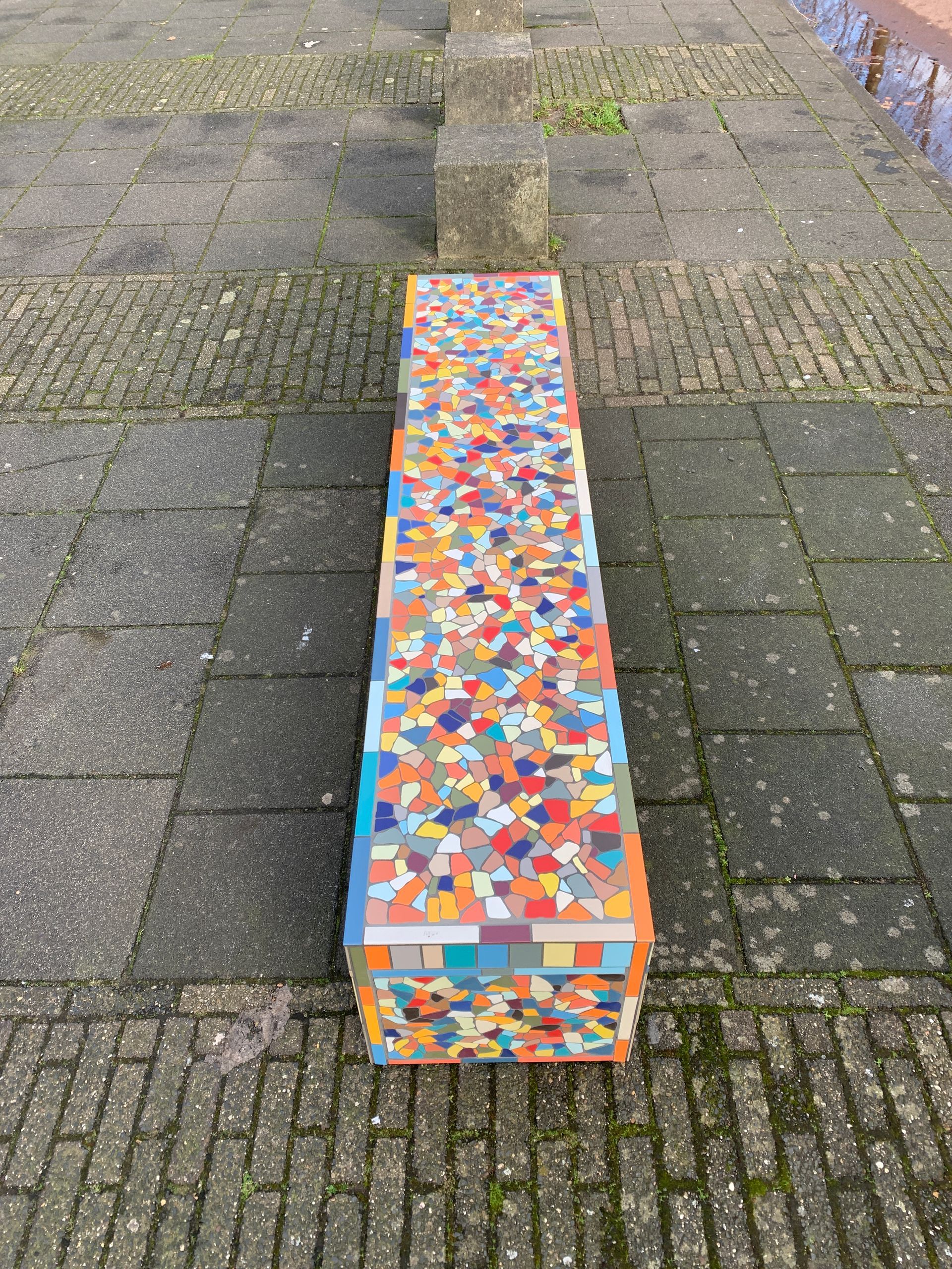Een kleurrijke, met mozaïek bedekte bank op een geplaveid pad buiten.