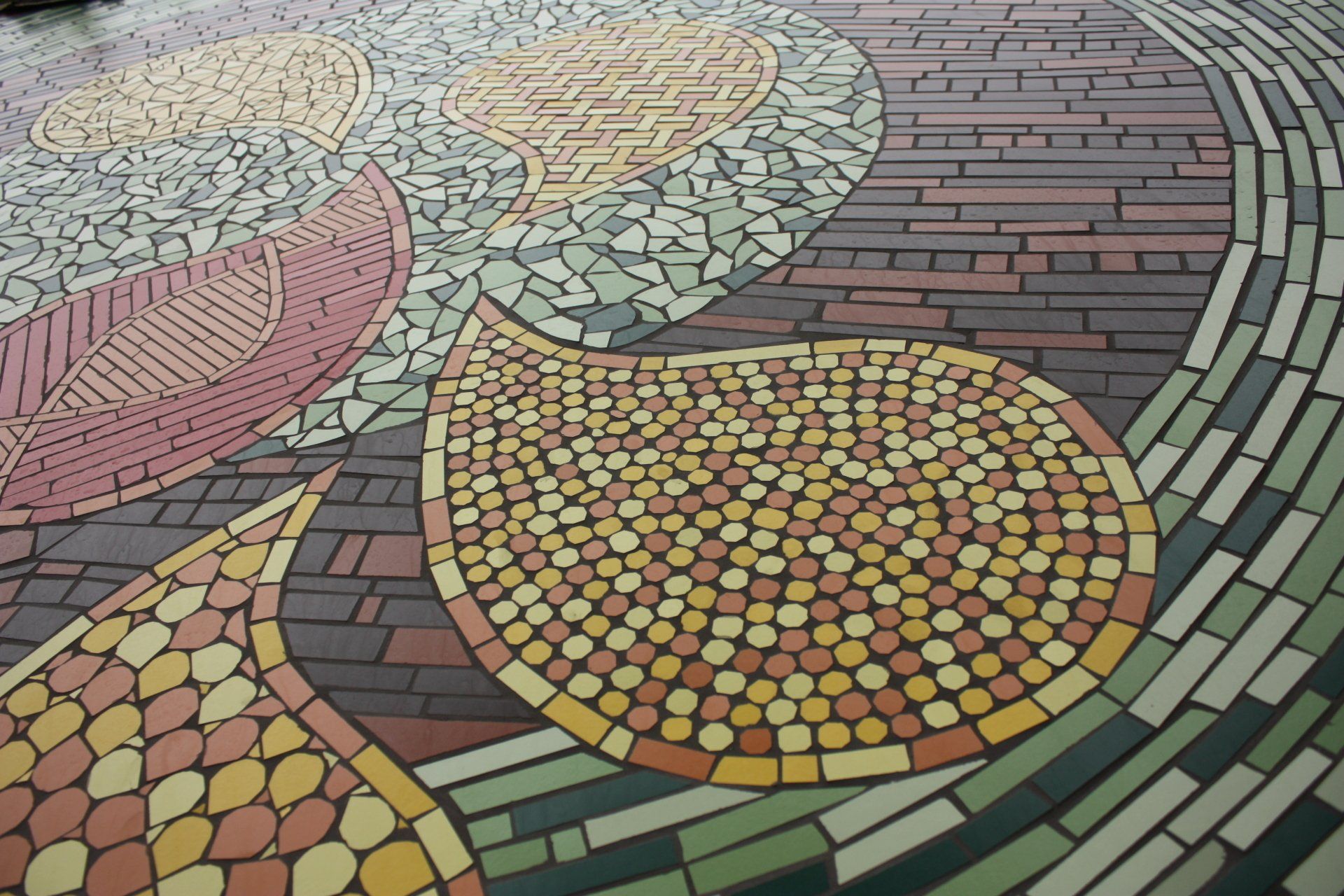 Kleurrijke mozaïekvloer met abstracte, gebogen patronen in roze, gele, groene en grijze tegels.
