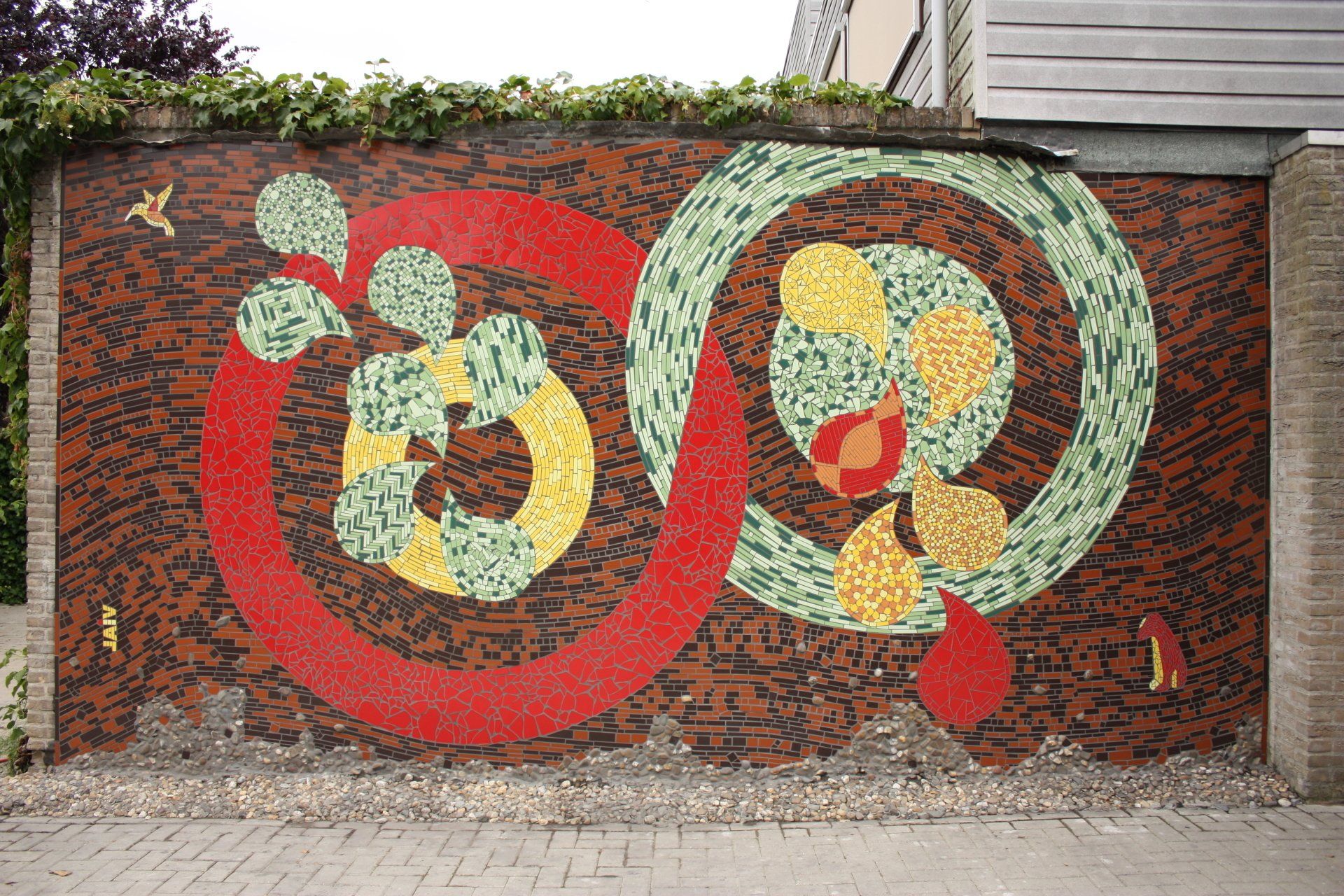 Kleurrijke muurschildering van overlappende rode en groene cirkels op een bakstenen muur met abstracte bloem- en bladvormen.