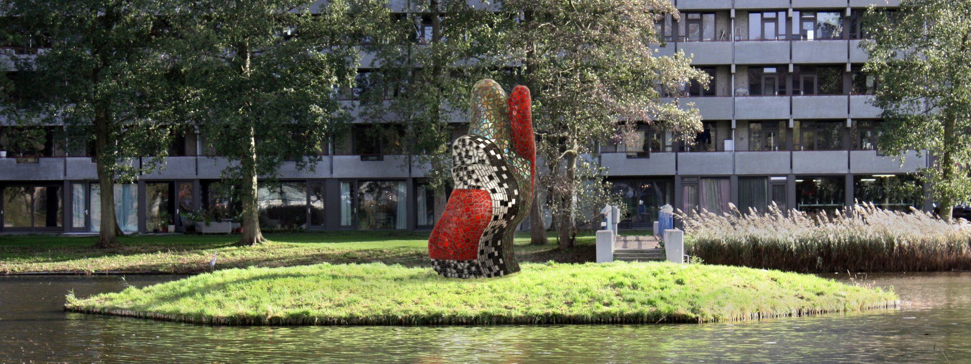 Een abstract beeld in rood en wit op een grasveld voor een appartementencomplex.