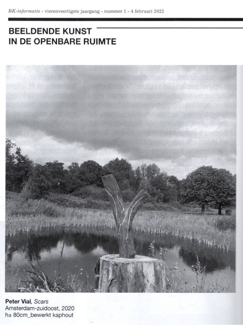 Zwart-witfoto van een sculptuur op een houten stronk bij een vijver, met bomen en een bewolkte hemel op de achtergrond.