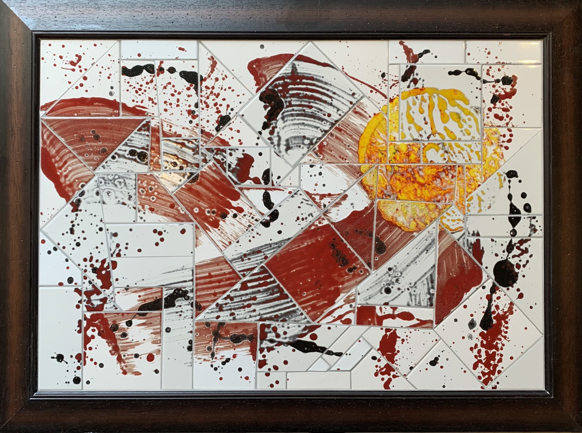 Abstract geometrisch schilderij met rode, oranje, gele en zwarte spetters in een donkere houten lijst.