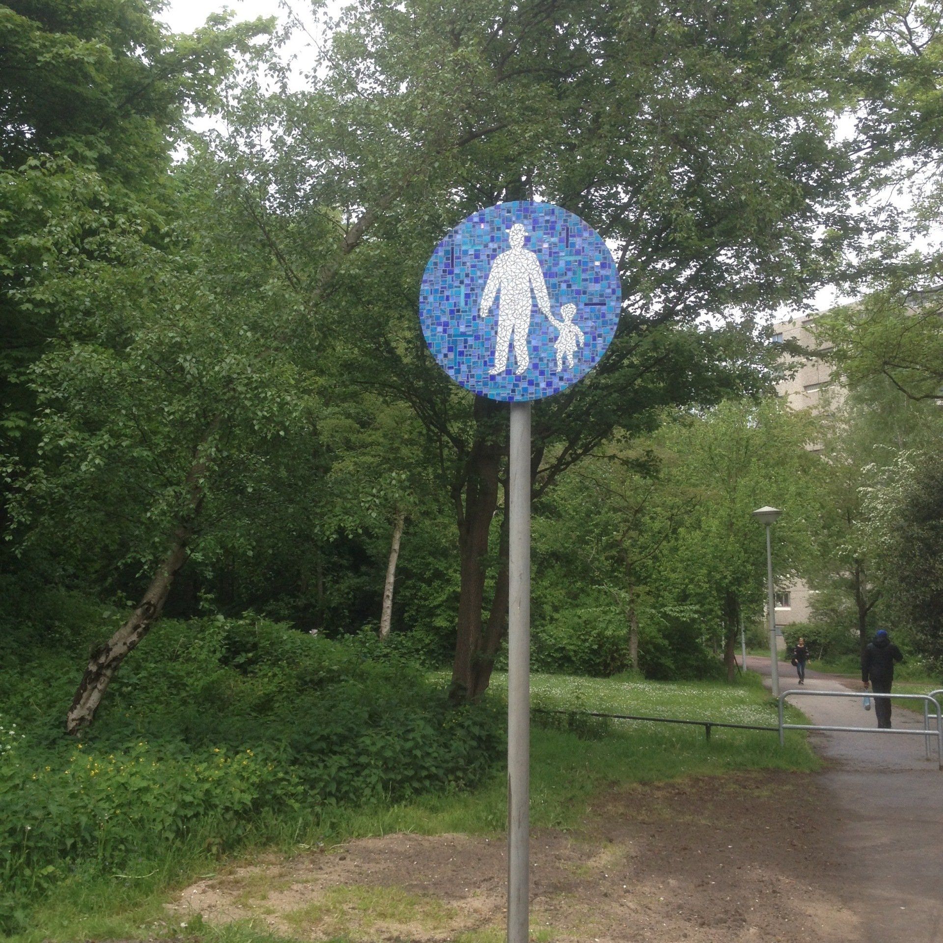 Blauw voetgangersoversteekbord op een paal langs een met bomen omzoomd parkpad.