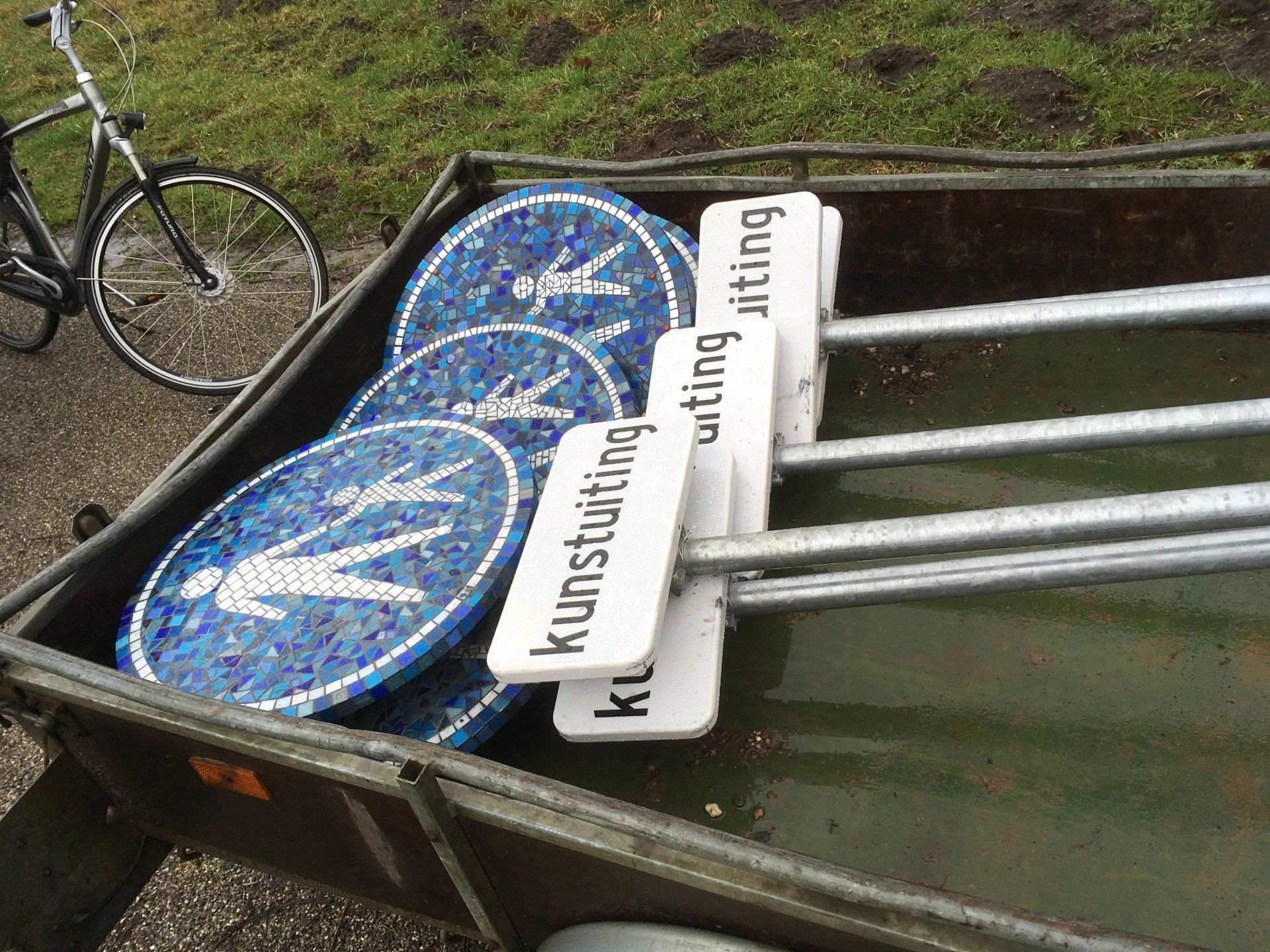 Blauwe huurfietsen in een zwarte aanhanger op het gras bij een fietswiel.
