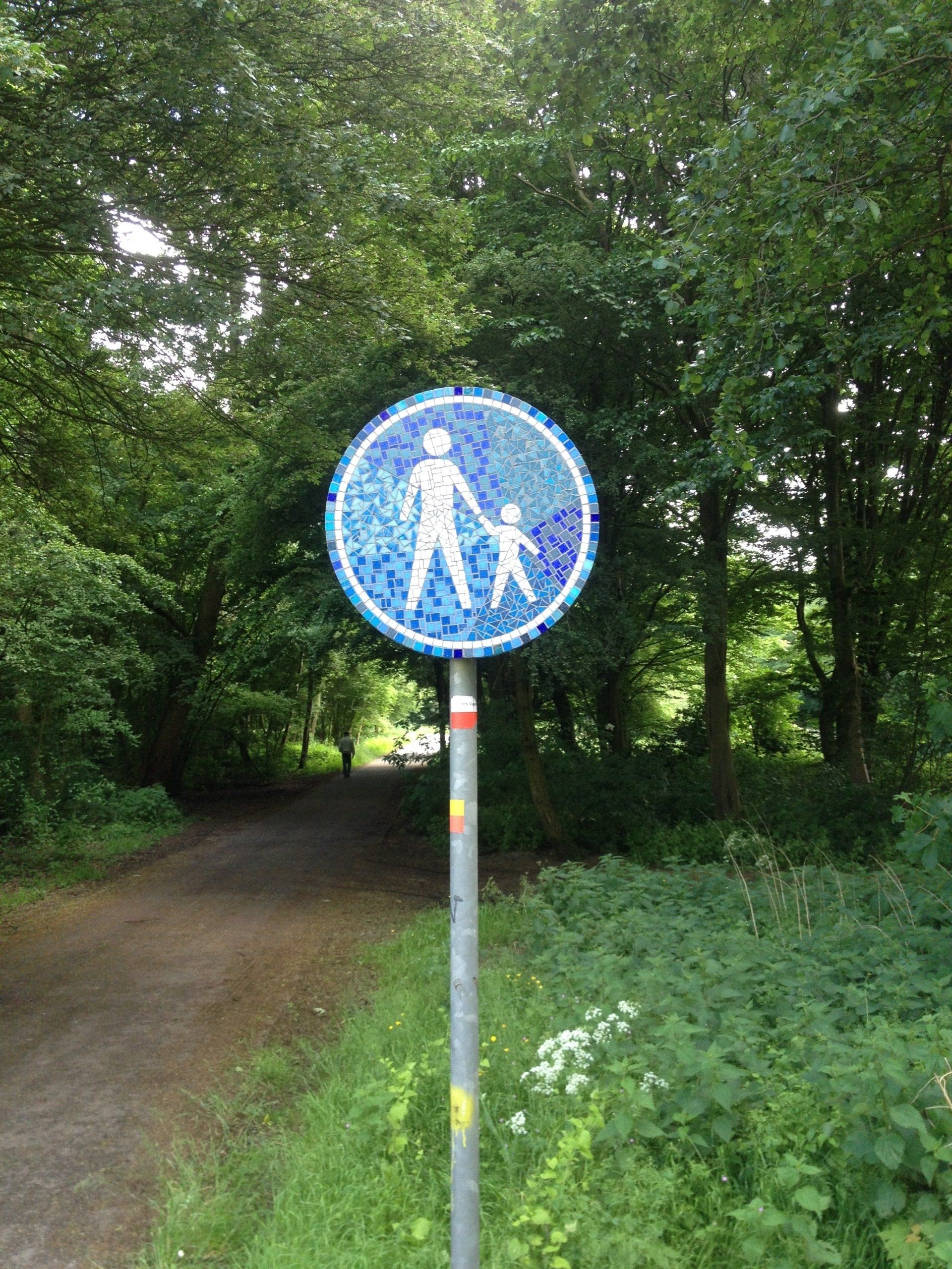 Blauw voetgangerspadbord op een paal langs een onverhard pad in het bos.
