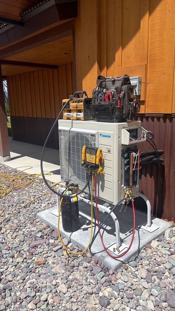 Outdoor HVAC/electrical unit with exposed wiring beside a wooden building on gravel