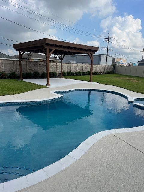 Swimming pool with a wooden pergola, surrounded by grass and a concrete patio.