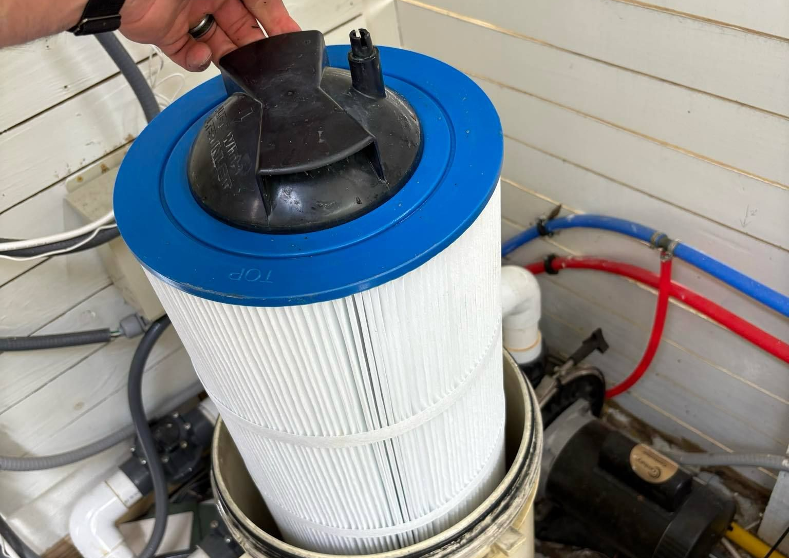 Man kneeling near a pool, working on a large black pool filter.