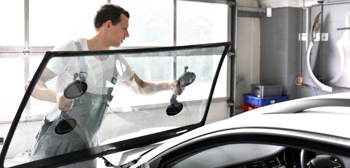 Worker cleaning a car windshield in a garage, using suction-cup tools on the glass