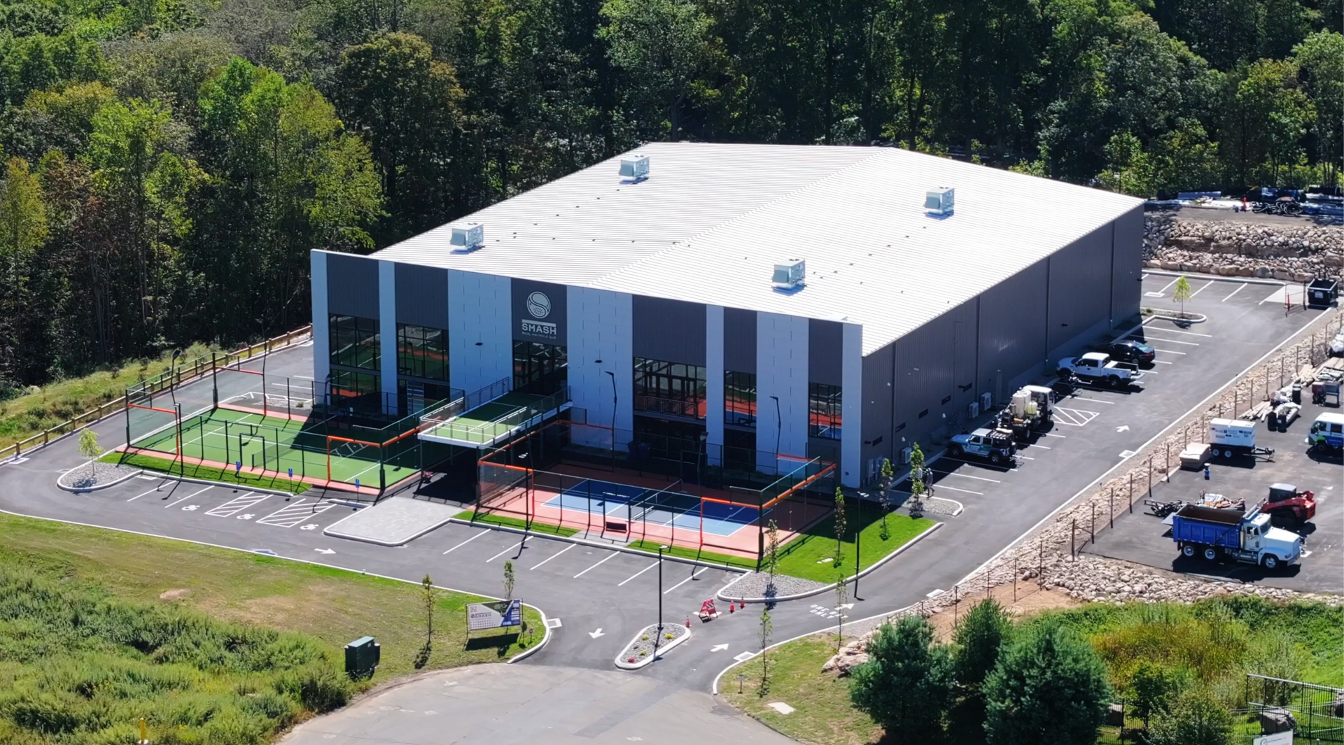 Aerial view of a large white industrial building with parking lots and surrounding greenery