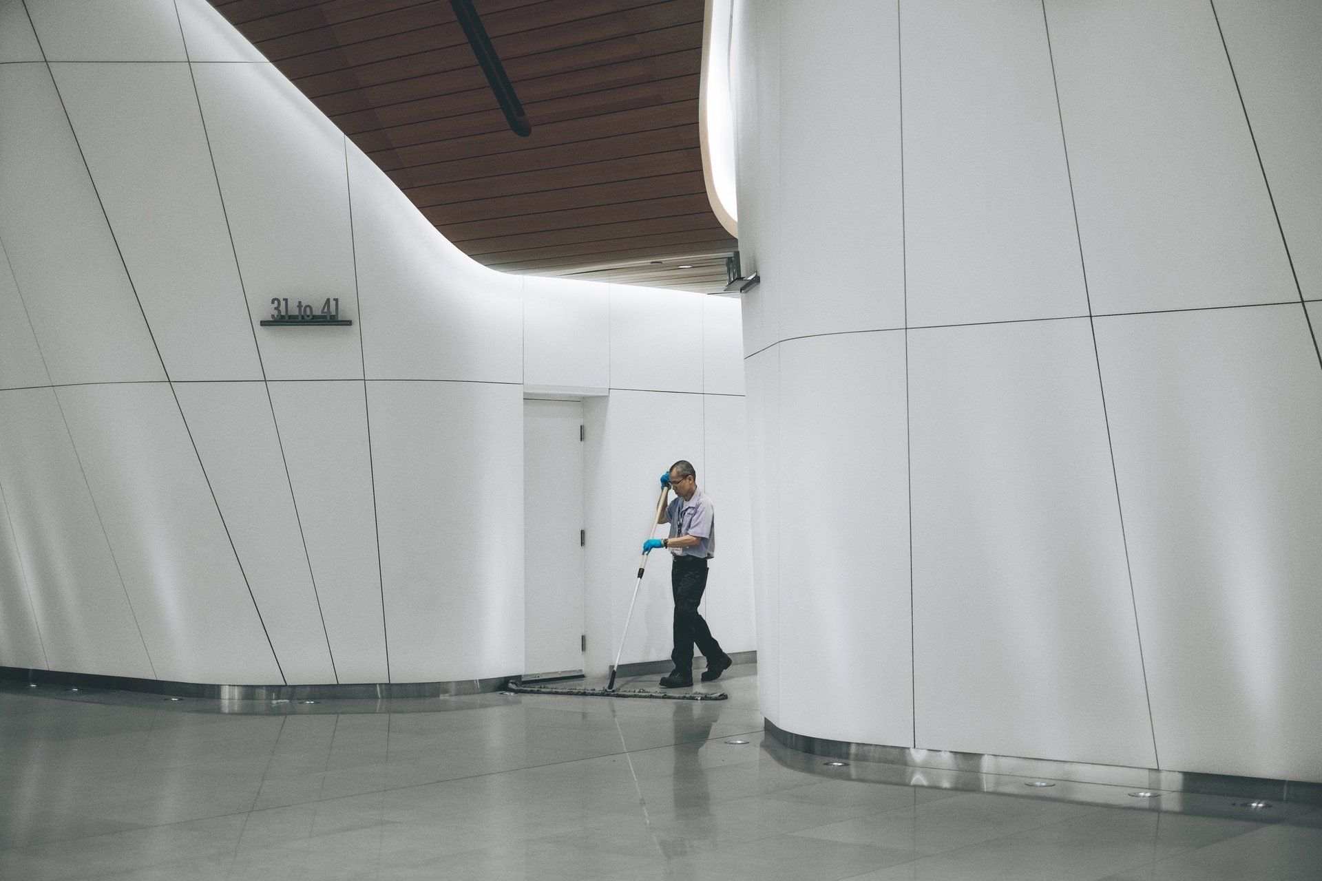 Person walking through a white, curved hallway with a door; modern architecture.