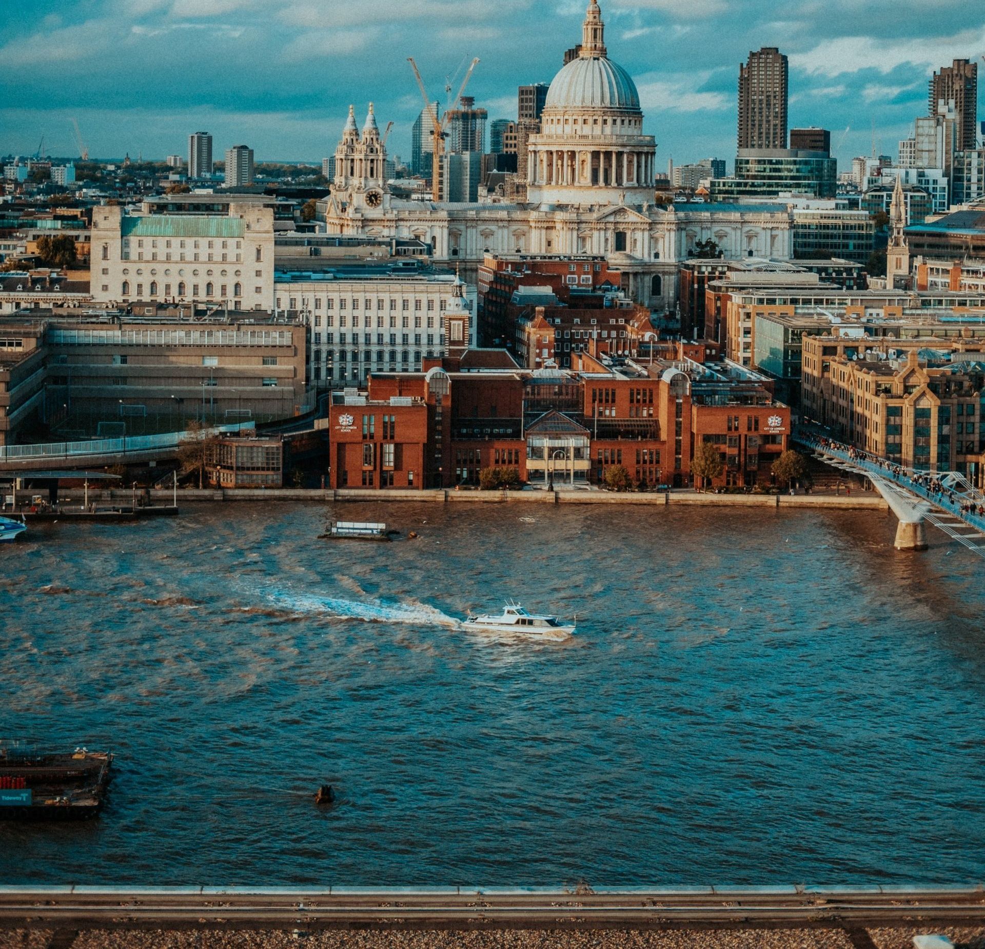 London cityscape: St. Paul's Cathedral, Thames River, boat, buildings, blue water, and sky.