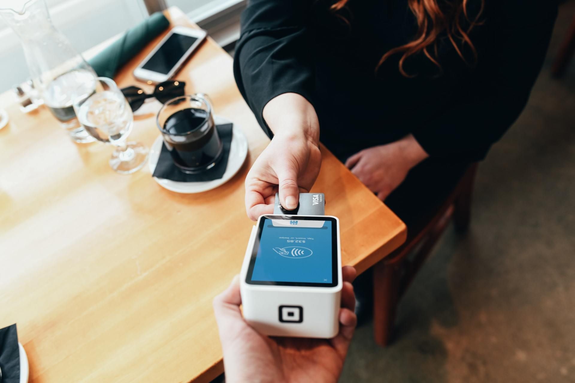 A person swipes a credit card on a payment device at a restaurant table.