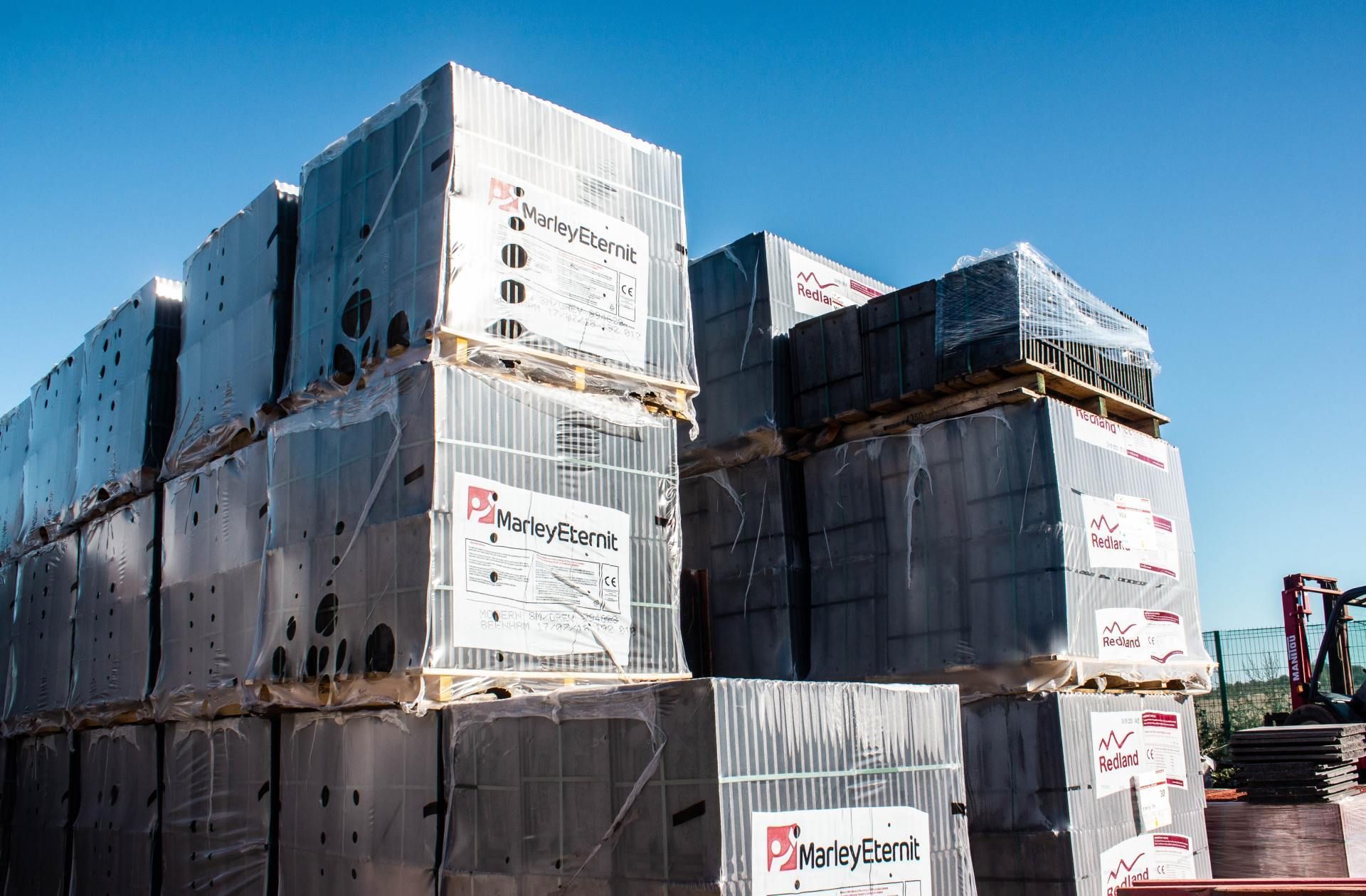 Pallets of wrapped construction materials stacked outdoors, blue sky.