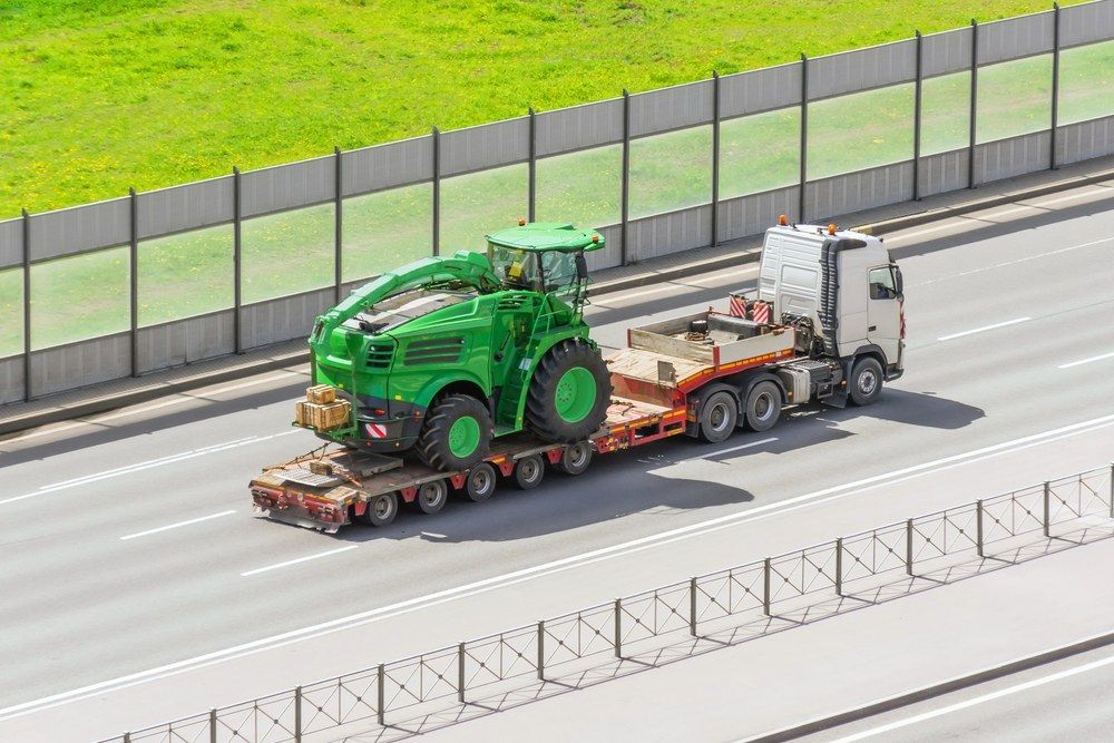 A Green Tractor is Being Transported on a Trailer on a Highway — Jammach Earthmoving in Muswellbrook, NSW