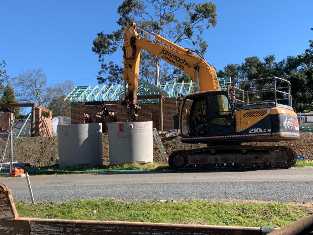 A Large Yellow Excavator is Parked on the Side of the Road — Jammach Earthmoving in Maitland, NSW