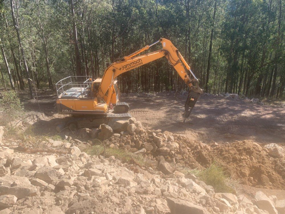 A Yellow Excavator is Working on a Pile of Rocks in the Middle of a Forest — Jammach Earthmoving in Singleton, NSW