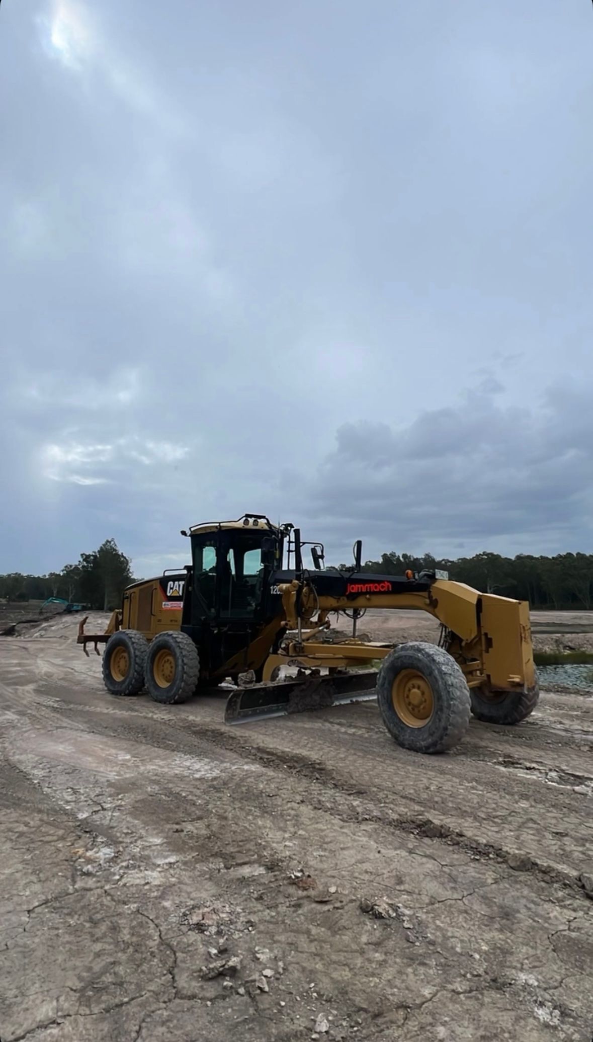 Yellow CAT grader on a dirt construction site under cloudy skies. — Jammach Earthmoving in Nulkaba, NSW