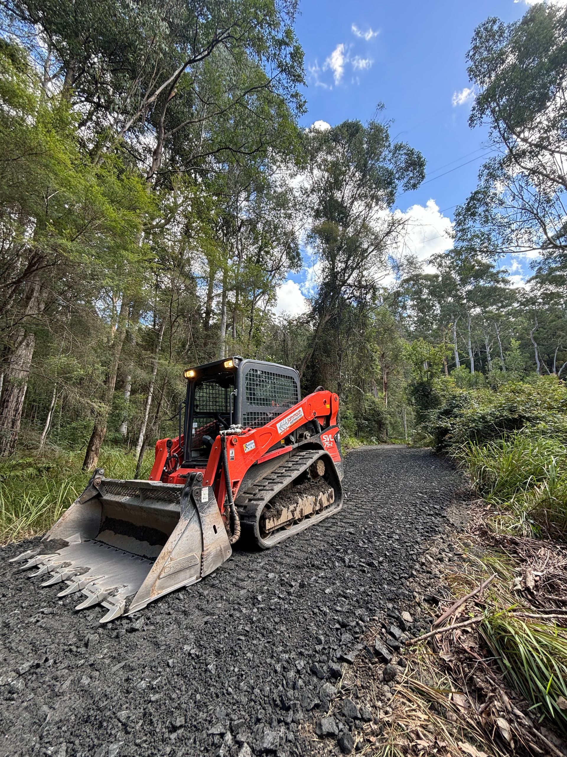Red skid steer loader grading a gravel road through a forested area. — Jammach Earthmoving in Nulkaba, NSW