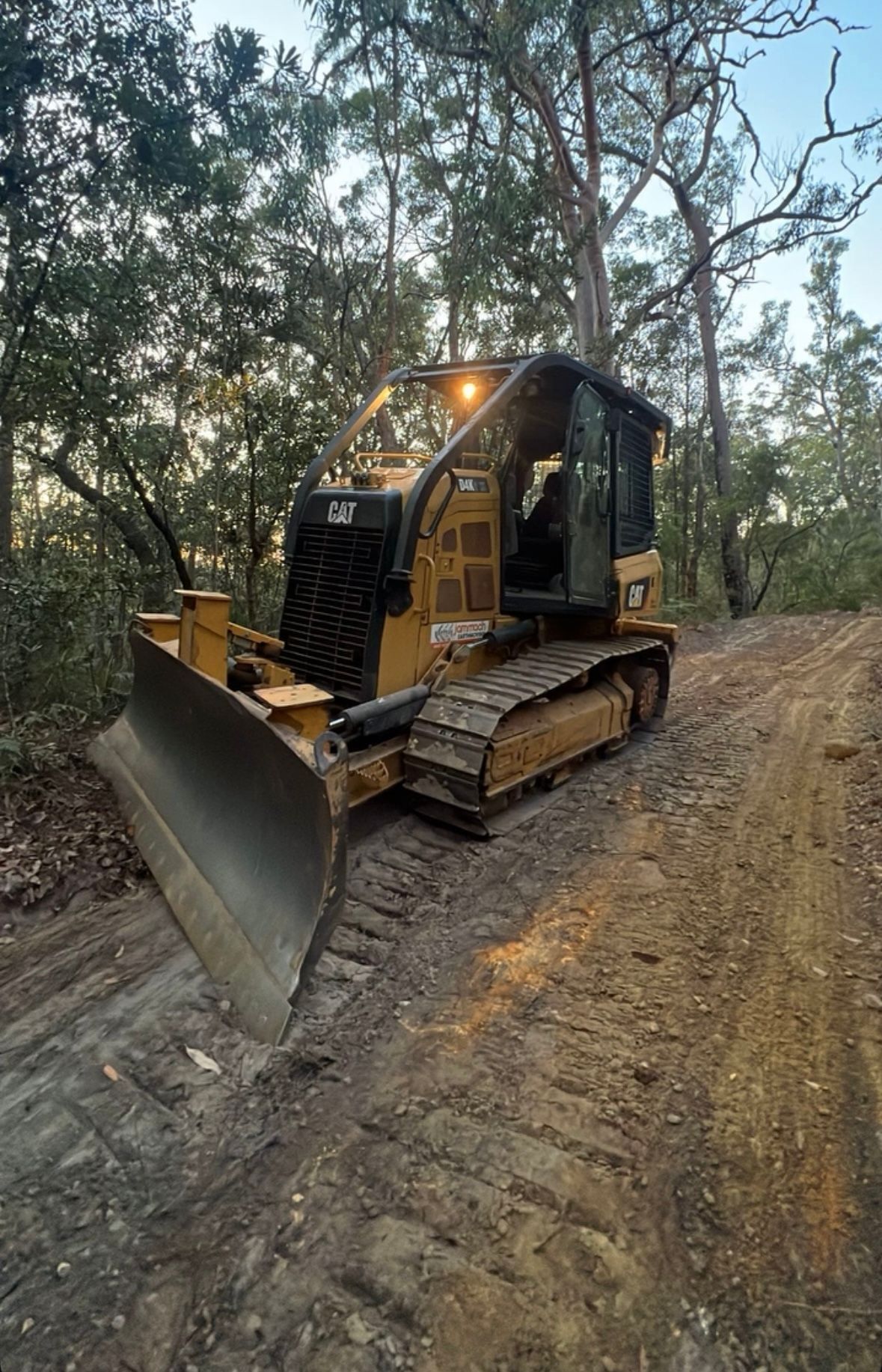 Yellow CAT bulldozer with tracks on a dirt trail in a forest at dusk.— Jammach Earthmoving in Nulkaba, NSW