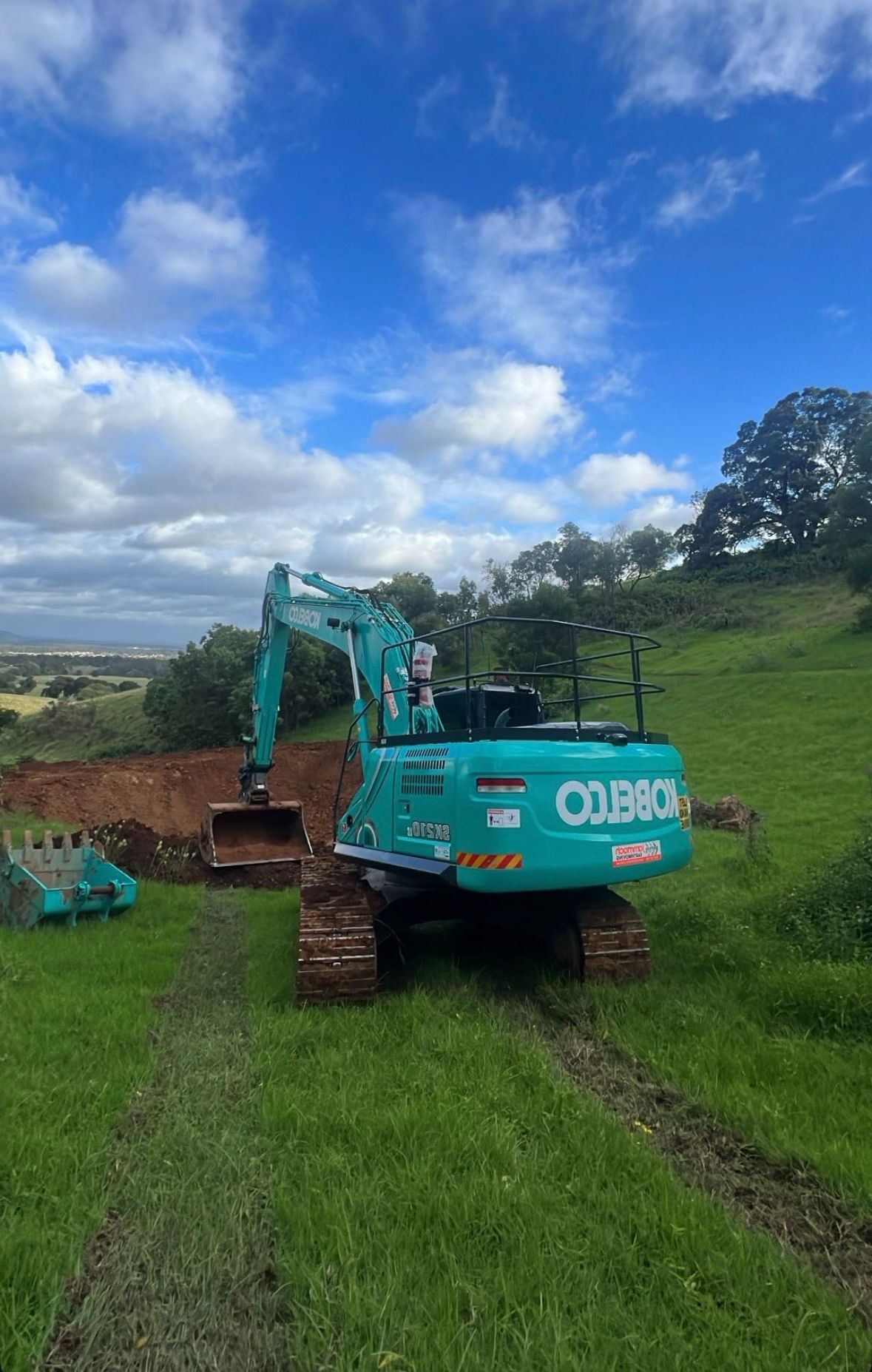 A Blue Excavator is Parked in a Grassy Field — Jammach Earthmoving in Nulkaba, NSW