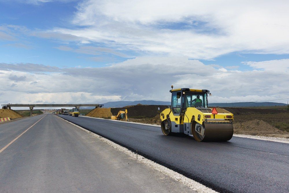 A Yellow Road Roller is Rolling Asphalt on a Road Under Construction — Jammach Earthmoving in Newcastle, NSW