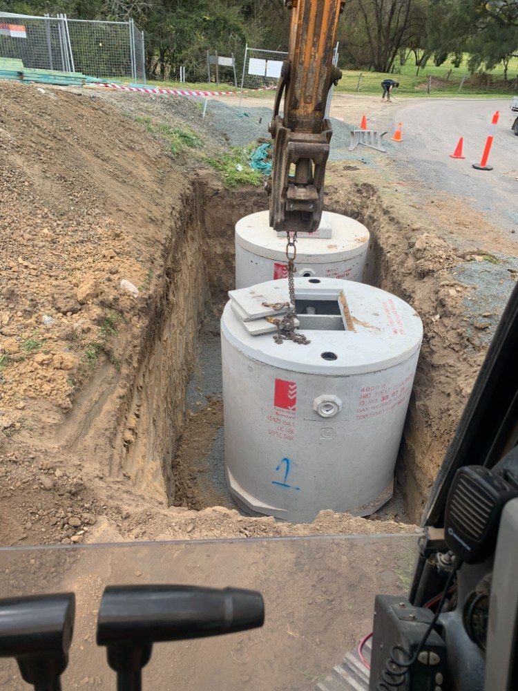 A Crane is Lifting Concrete Cylinders Into a Hole in the Ground — Jammach Earthmoving in Maitland, NSW