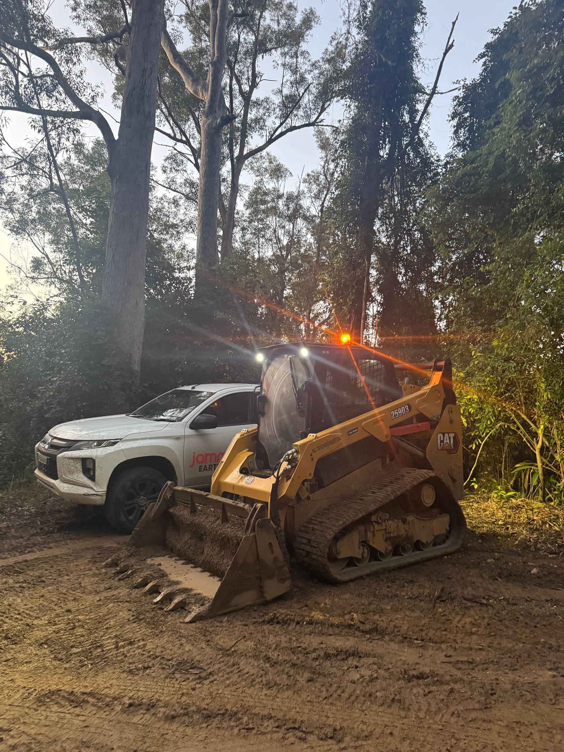 A Bulldozer is Parked Next to a White Truck in a Dirt Lot — Jammach Earthmoving in Nulkaba, NSW