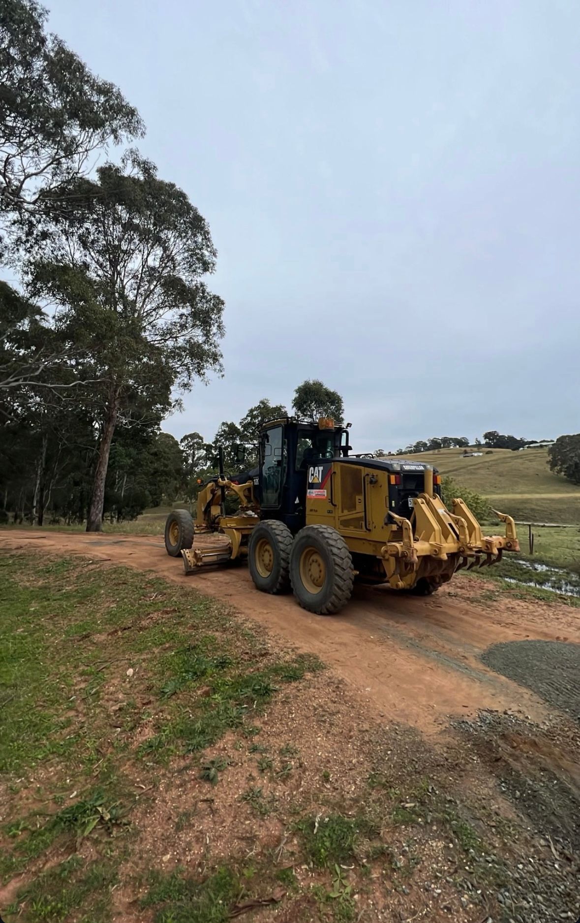 A Yellow Tractor is Driving Down a Dirt Road — Jammach Earthmoving in Nulkaba, NSW