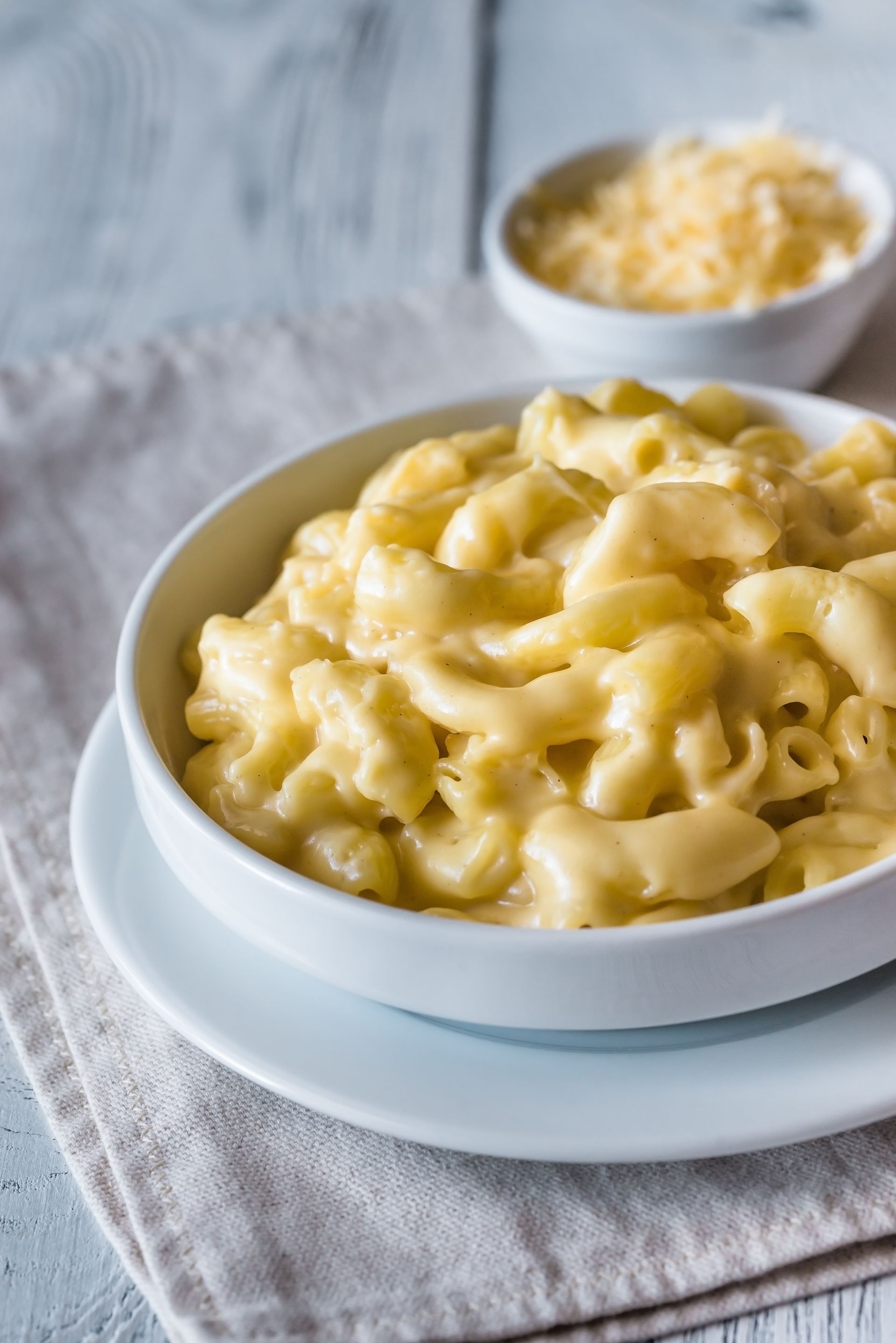 Mac and cheese in a white bowl, with grated cheese in a small bowl behind it.