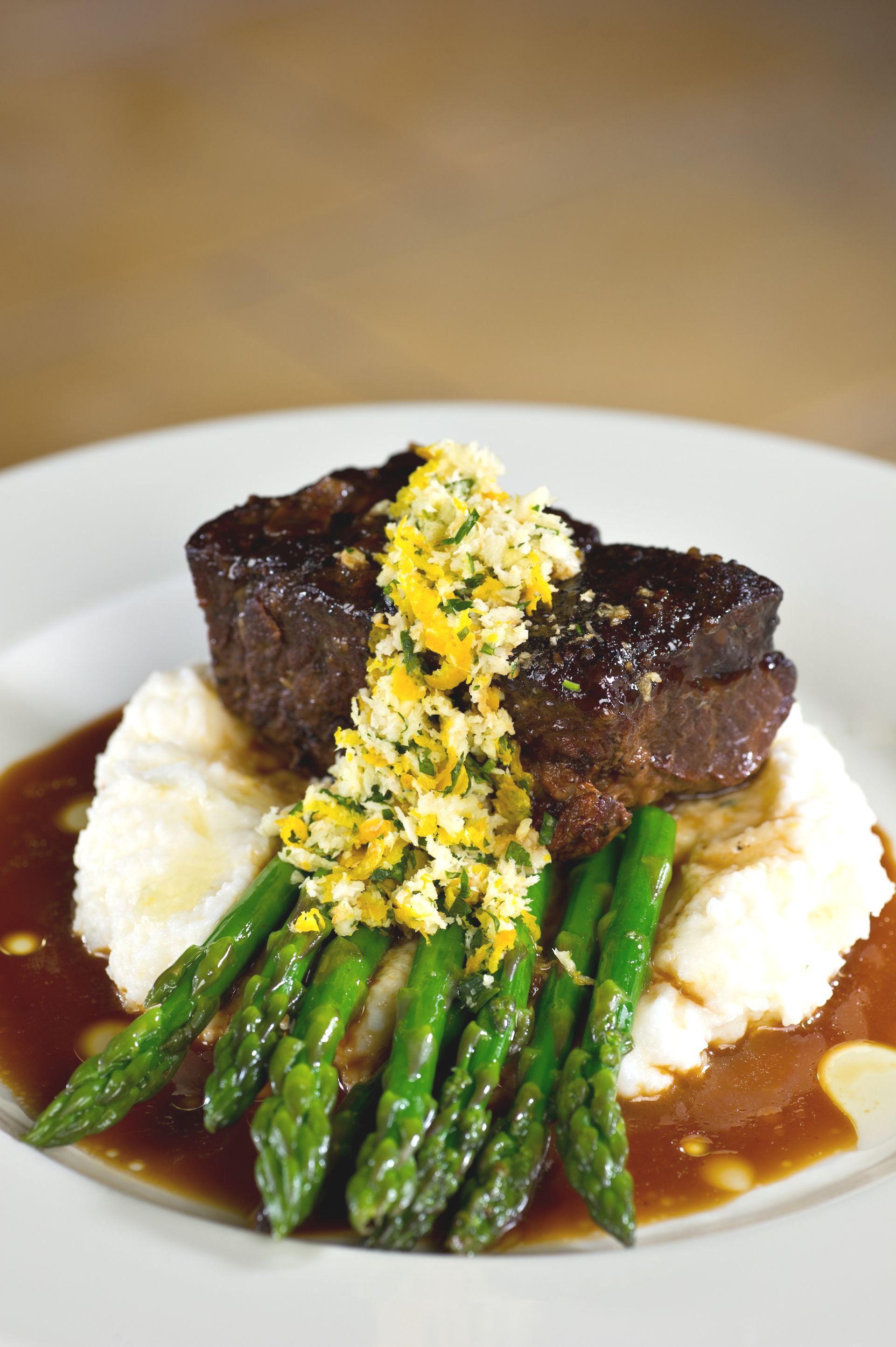 Filet mignon with asparagus, mashed potatoes, and sauce on a white plate.